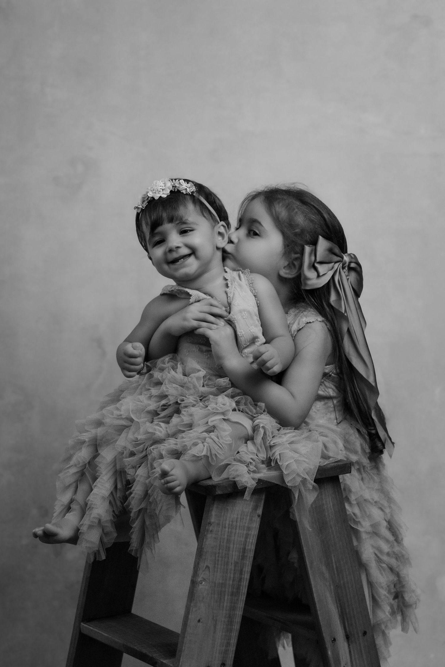 Black and white photo sequence showing two children in playful interaction with a feather boa accessory.