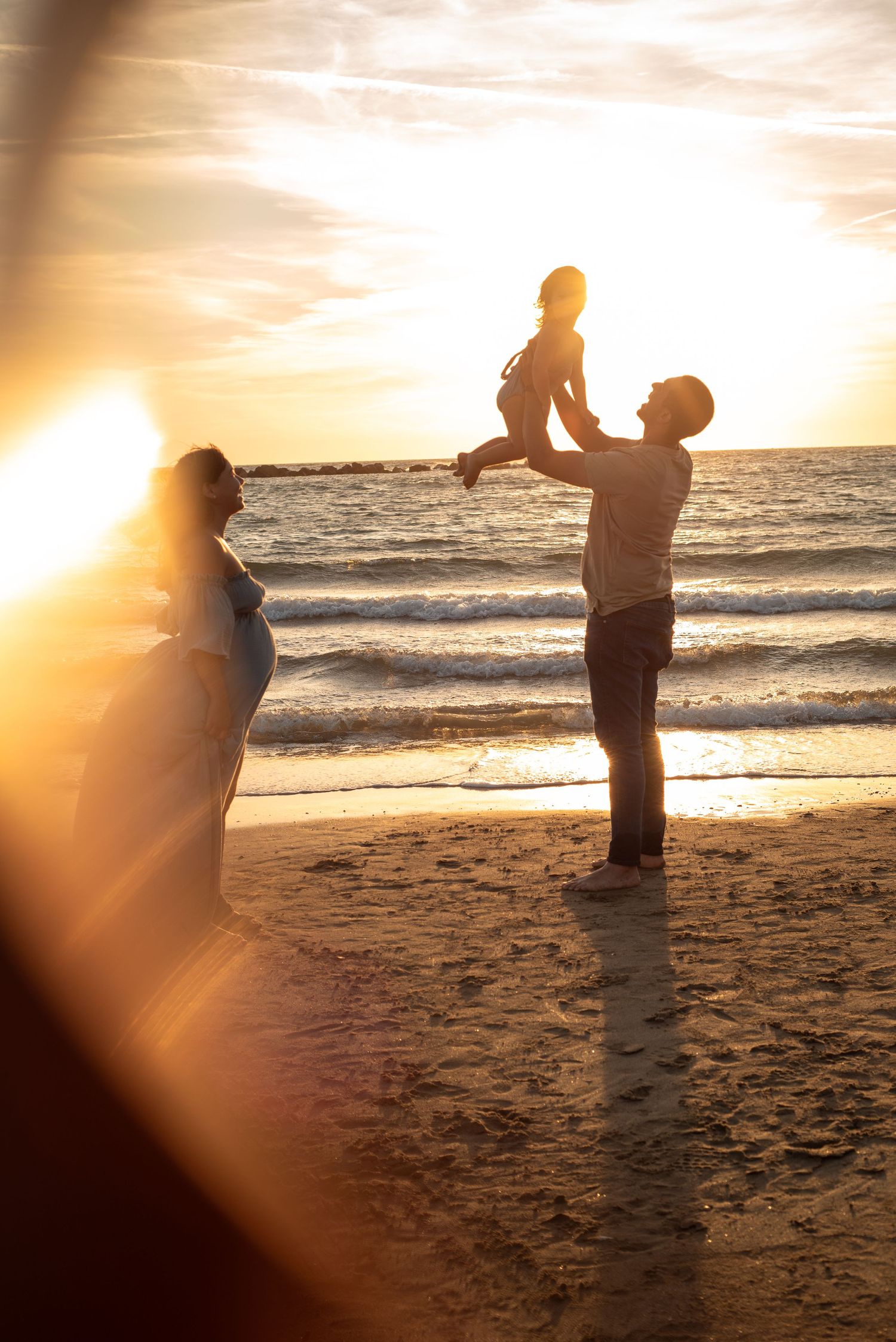Silhouettes of people on a beach at sunset with dramatic golden sunlight creating a warm, ethereal atmosphere.