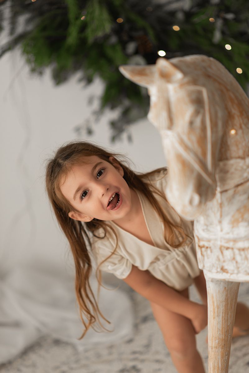 A child drinks a chocolate milkshake with a straw while standing near a Christmas tree with twinkling lights.