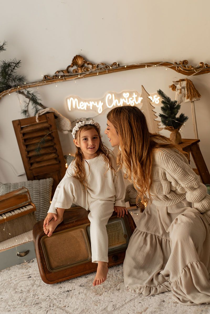 A cozy Christmas photo session featuring white knit sweaters and dresses against a rustic brown chair and white backdrop.