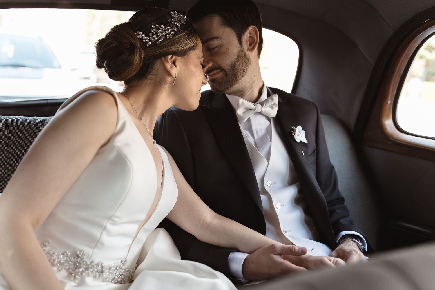 Bride and groom share intimate moments in the back of a vintage car on their wedding day.