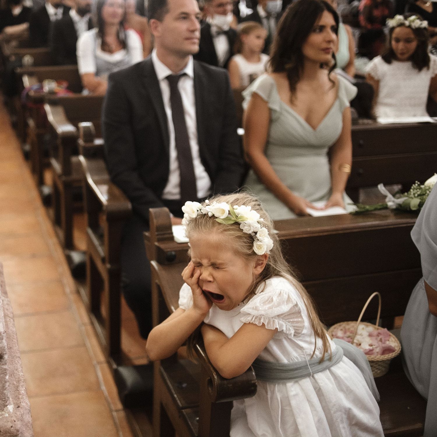 Wedding guests seated in church pews watch as a flower girl in white dress walks down the aisle during ceremony.