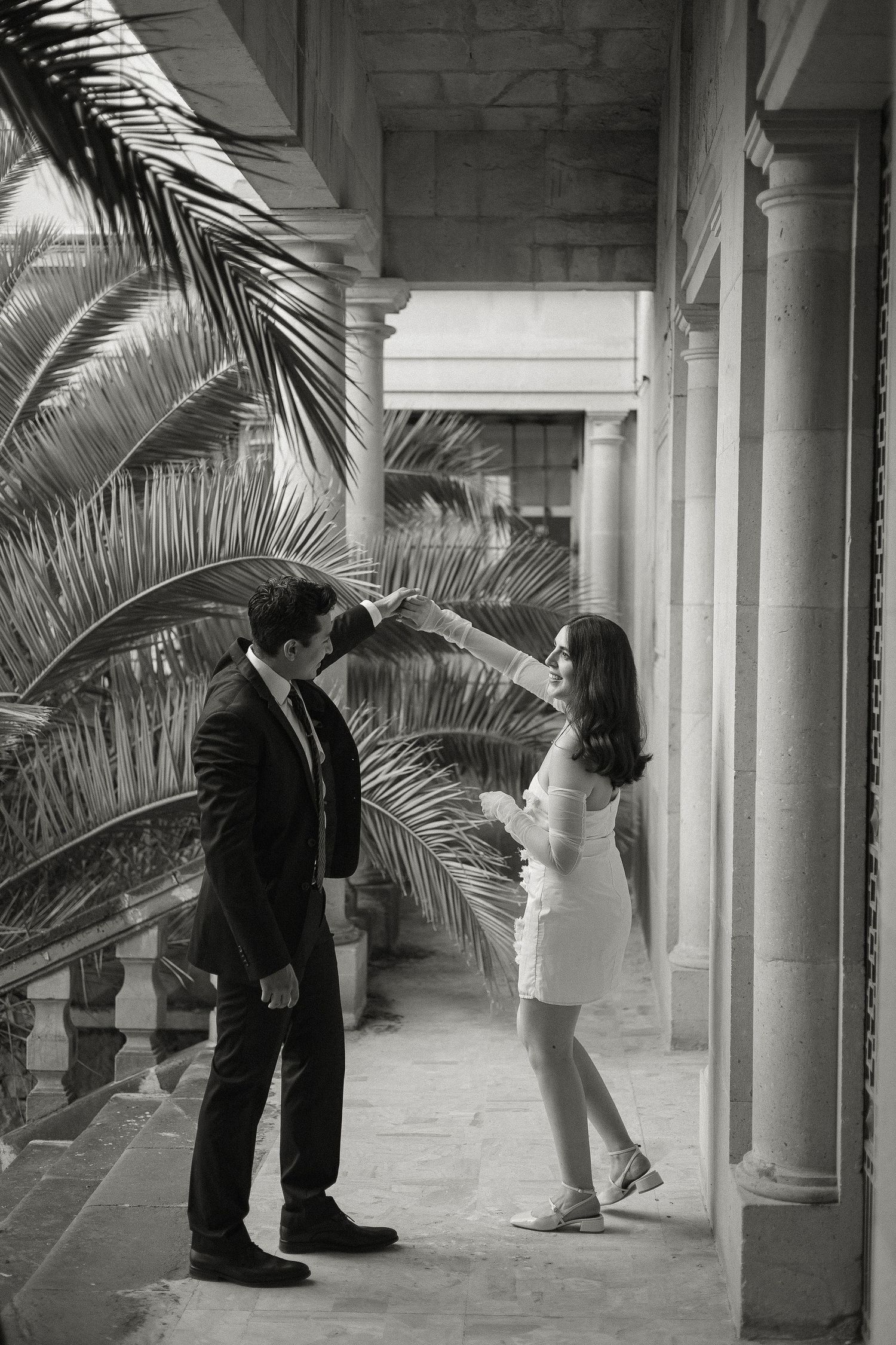 A sequence of black and white photographs showing someone bending down in a columned hallway with palm plants.