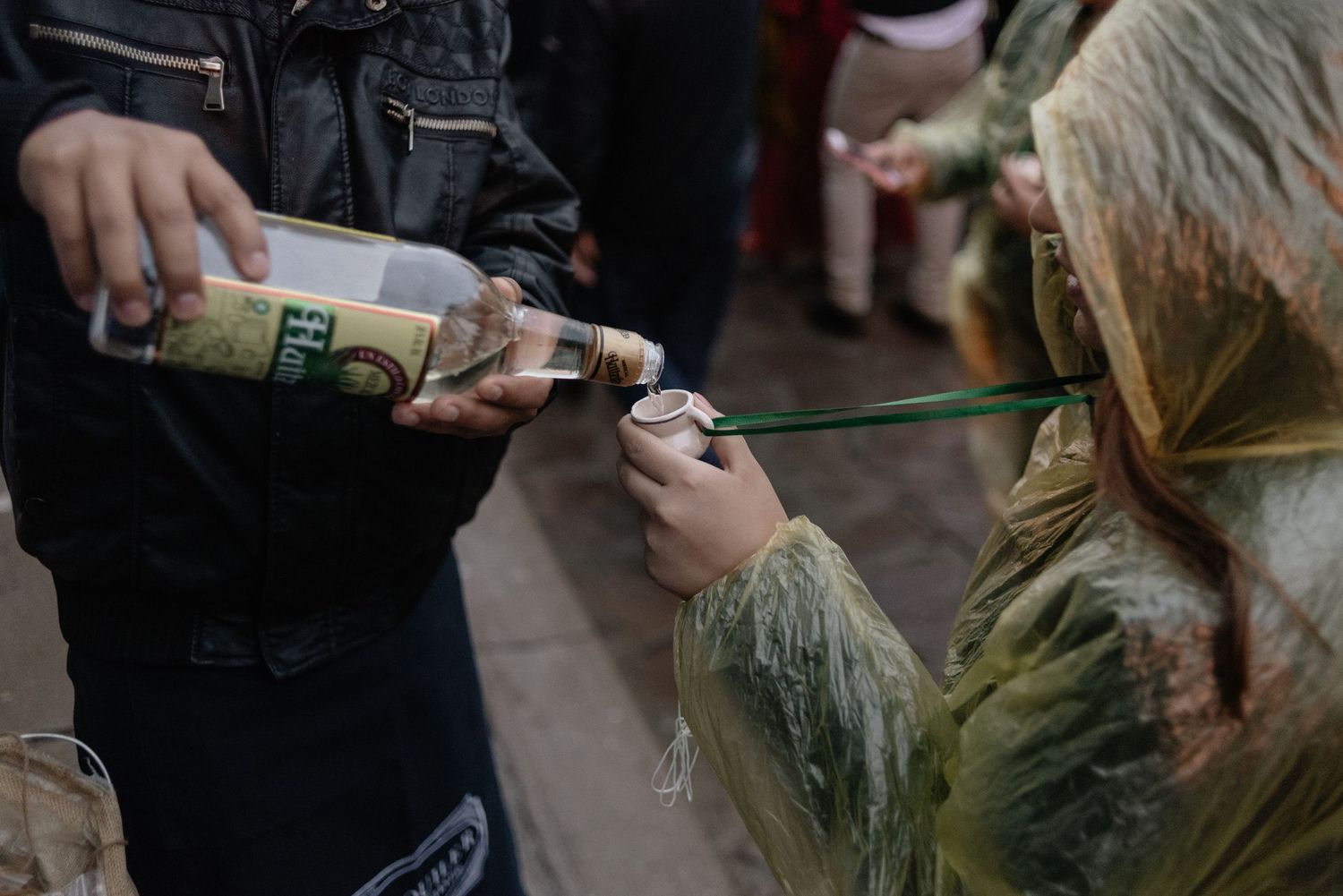Someone pours alcohol into a small glass during a social gathering outdoors.