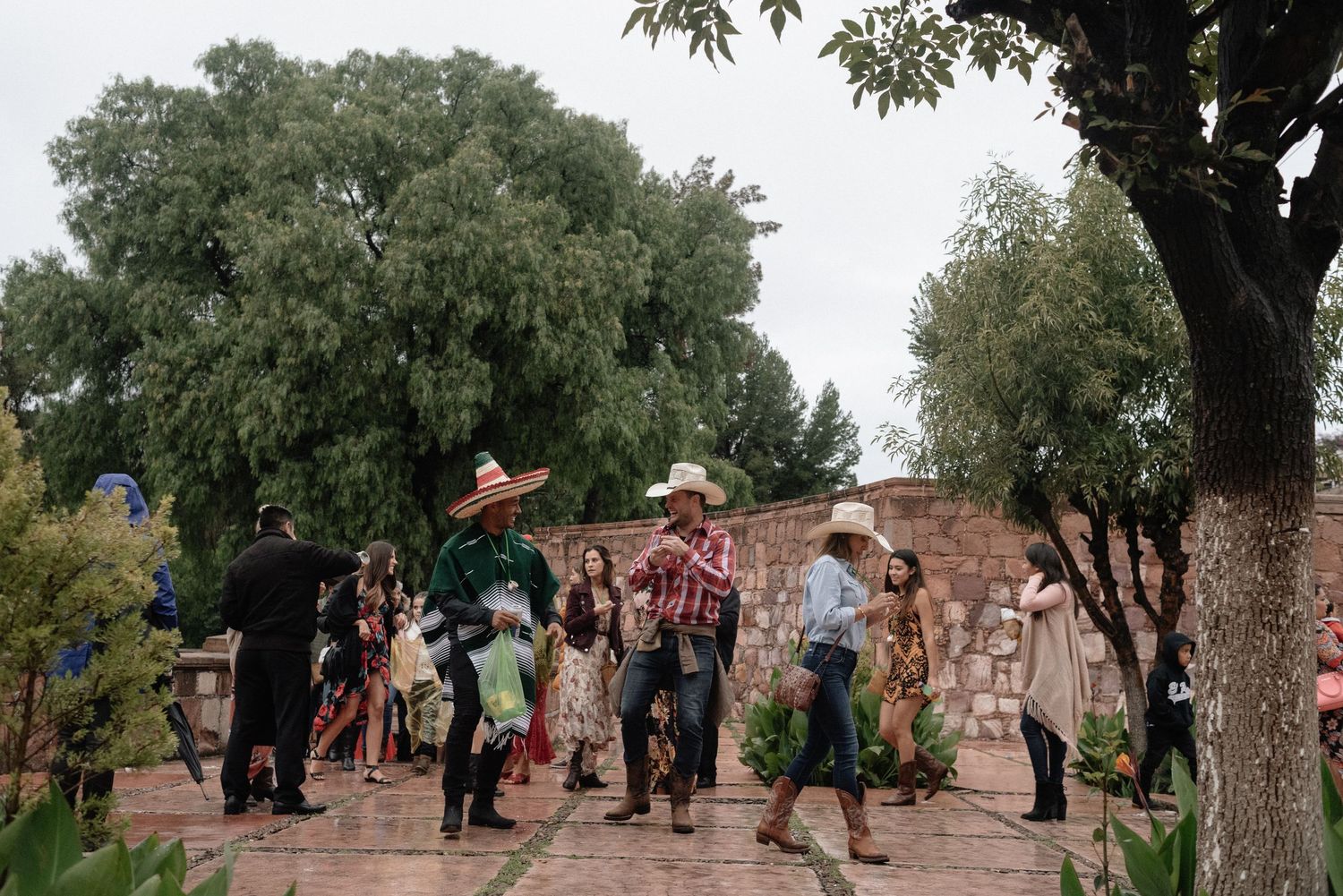 A group of people walking along a stone path surrounded by lush trees with ancient brick walls in the background.