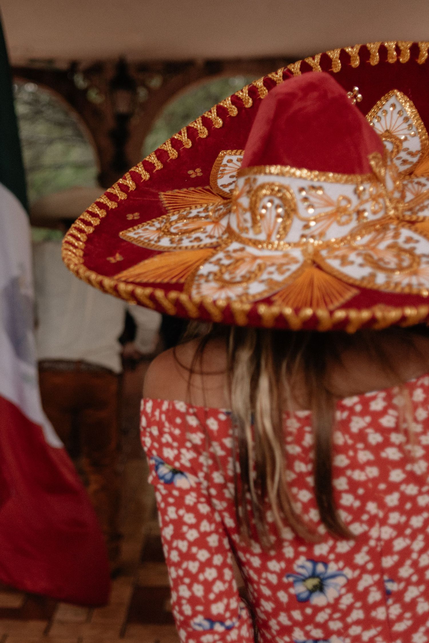 A decorative red and gold Mexican sombrero hat with ornate embroidery detail is worn above a floral print dress.