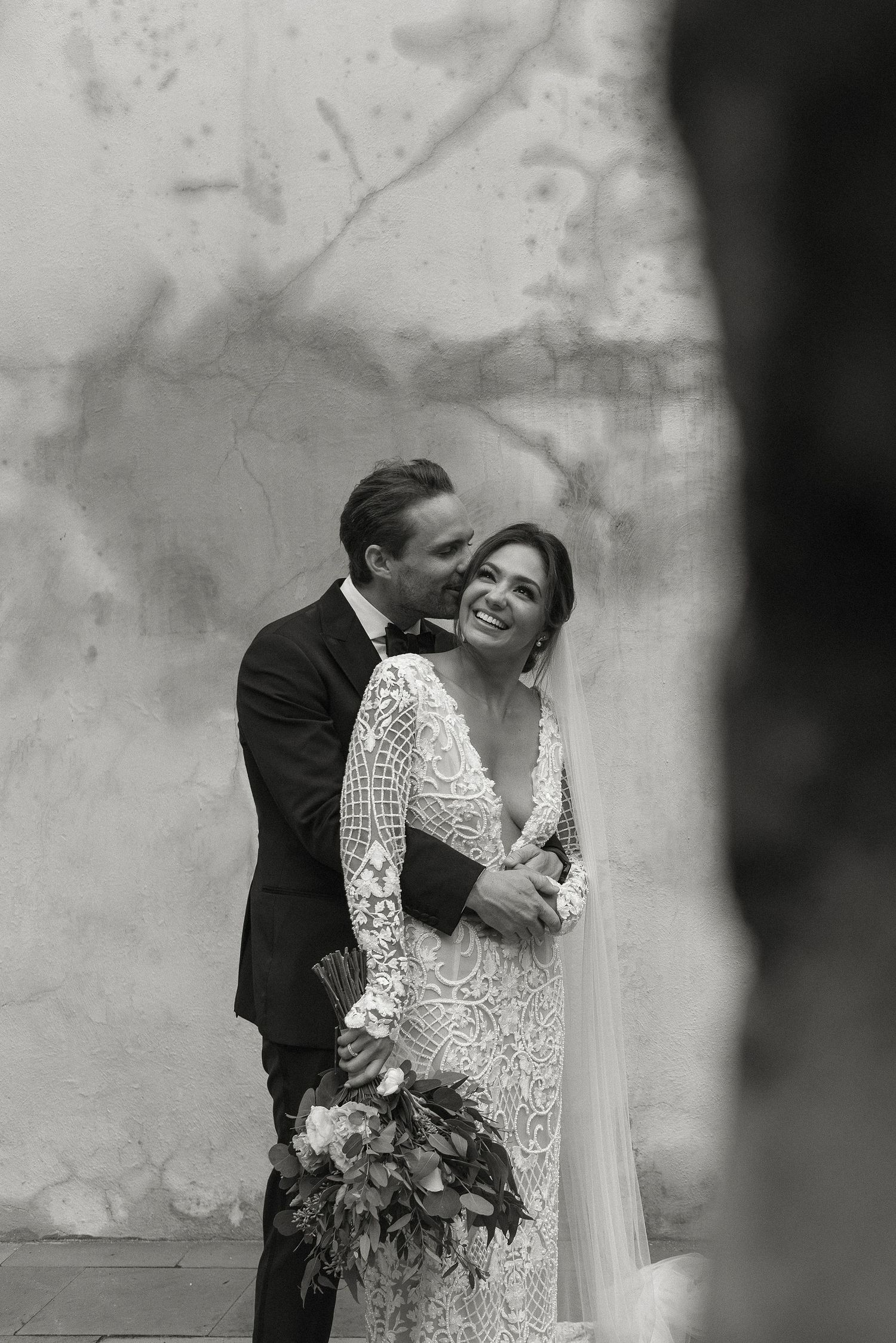 A tender black and white wedding portrait of a couple embracing, with the bride wearing an elegant lace gown.