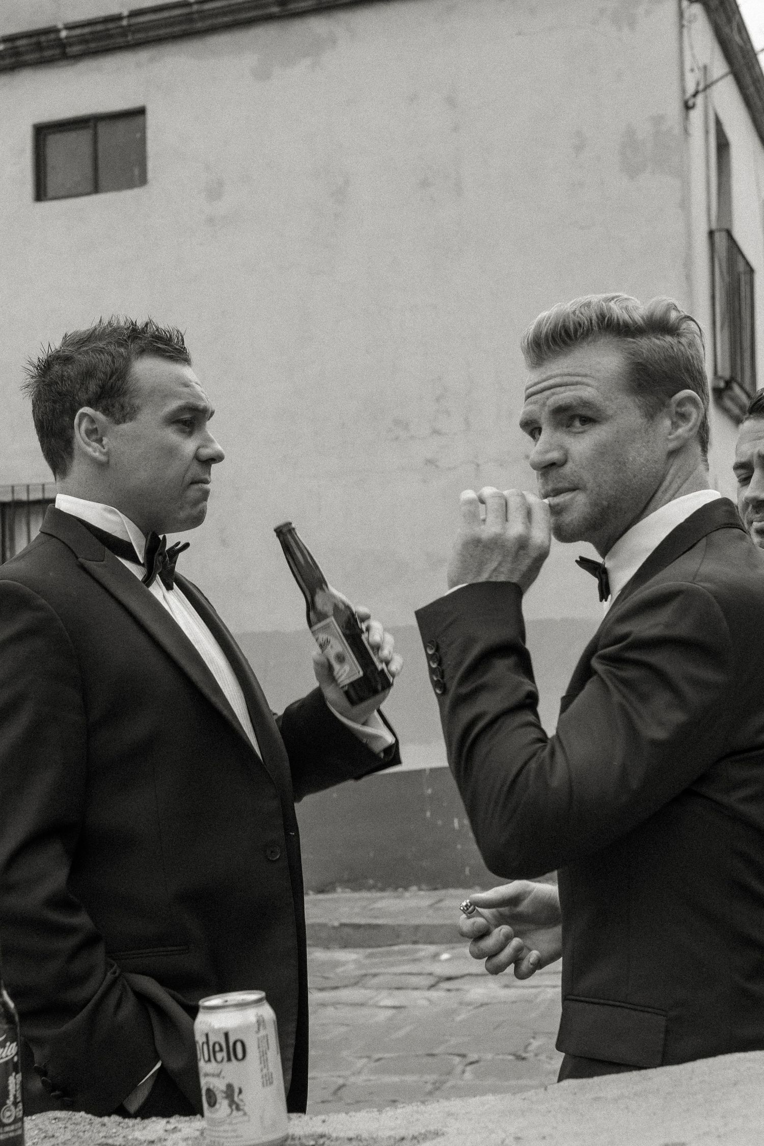 Two men in formal suits converse while holding drinks in a vintage black and white photograph.
