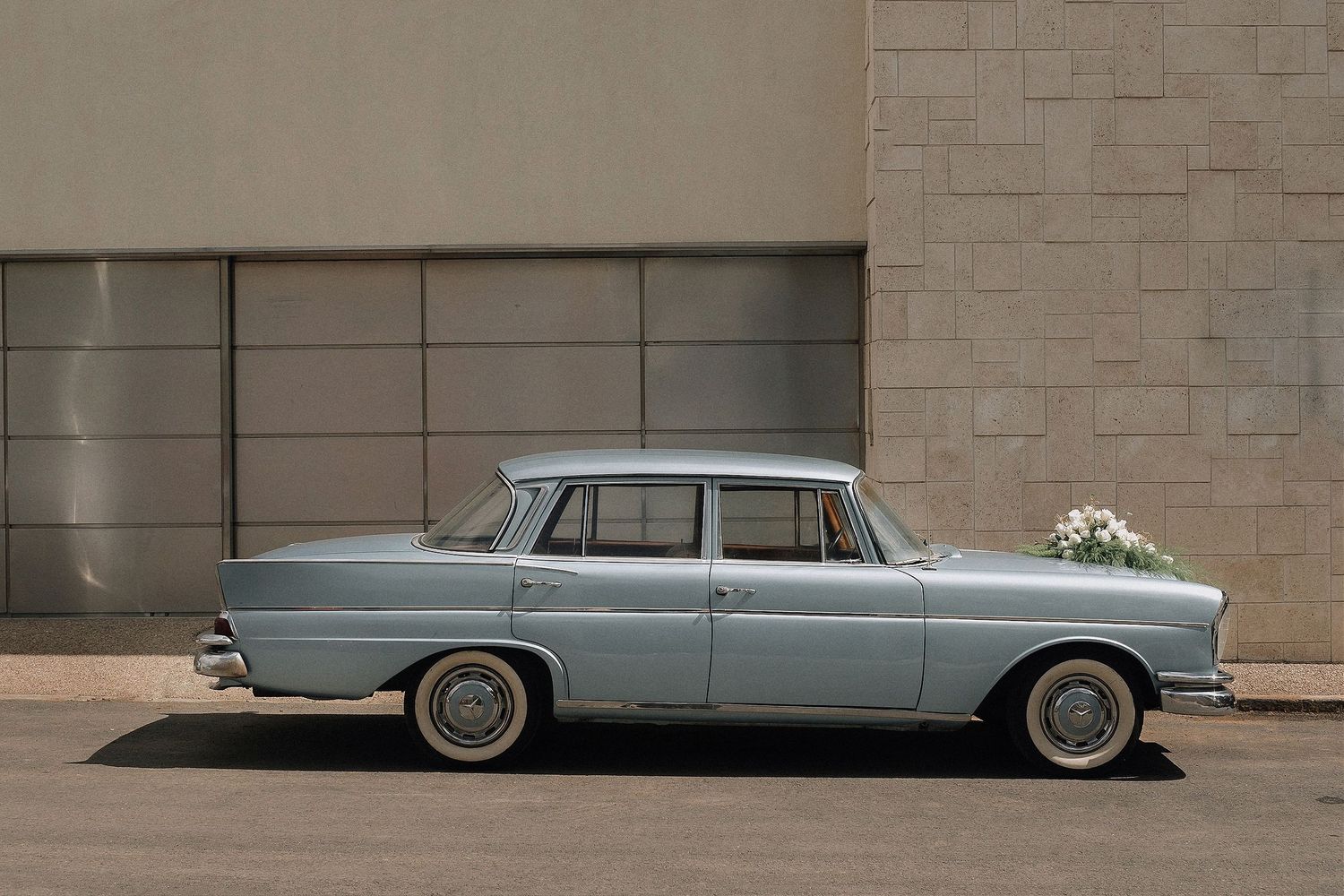 Classic light blue vintage car decorated with wedding flowers parked against modern wall.