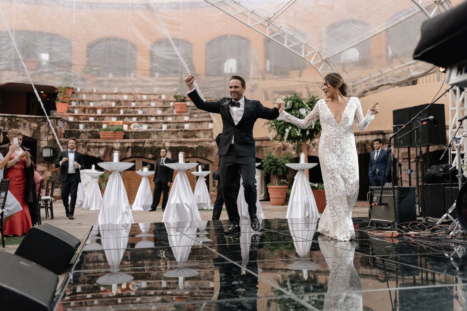 Joyful couple celebrates on reflective dance floor at elegant brick courtyard wedding reception venue.