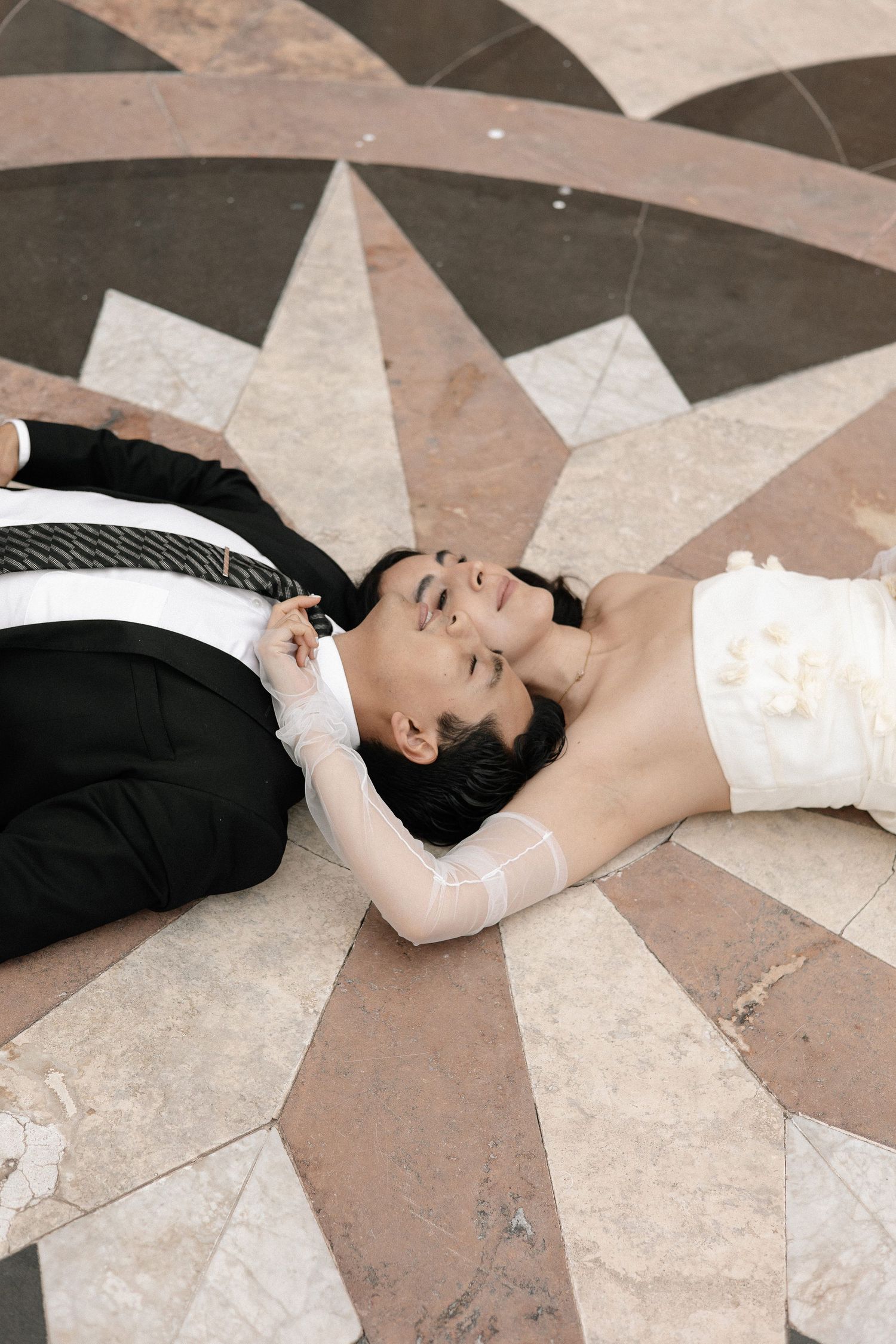 A person wearing a white dress lies on a geometric patterned floor in an artistic pose.