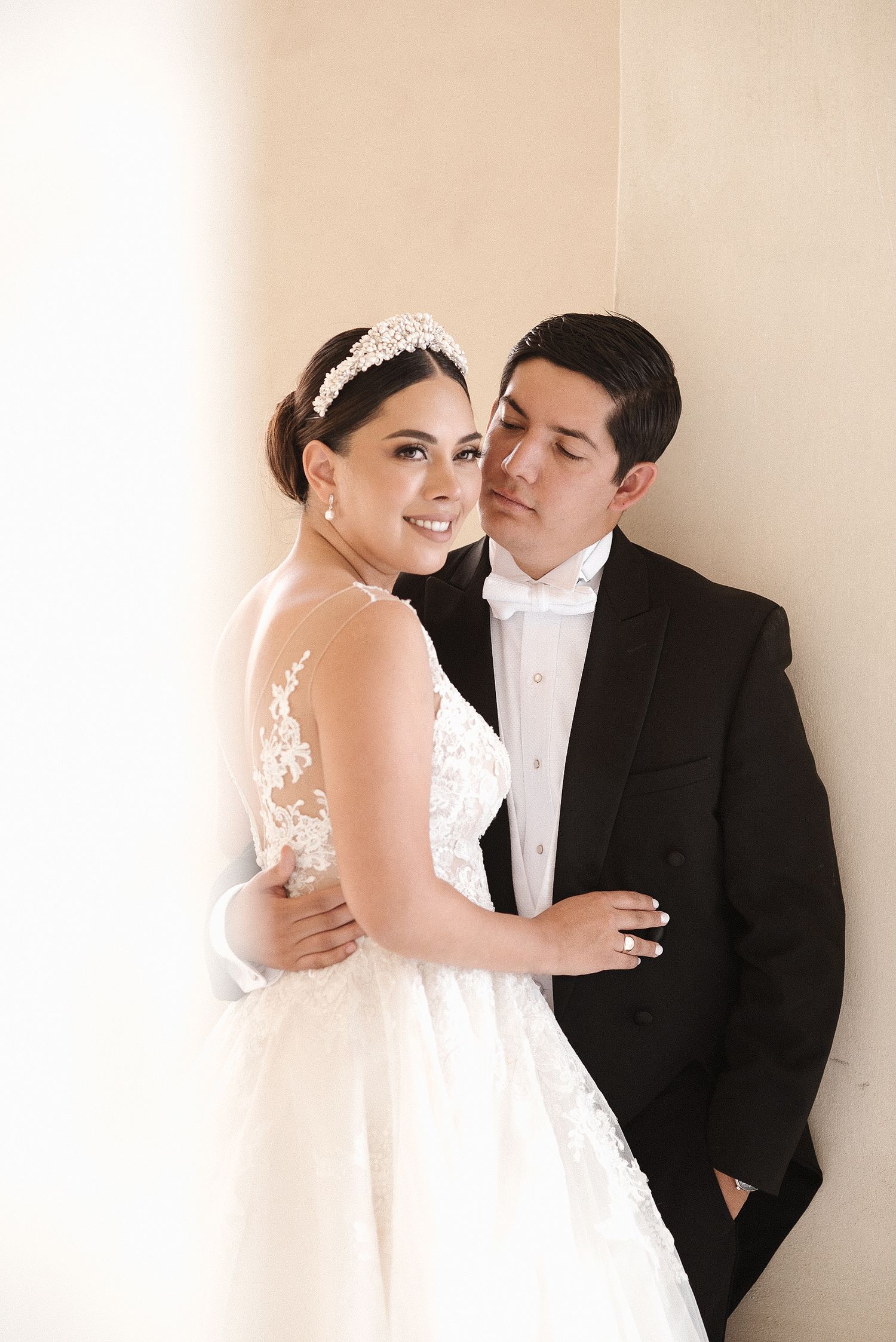 An elegant wedding portrait featuring a bride in a lace gown and groom in classic black tie attire.