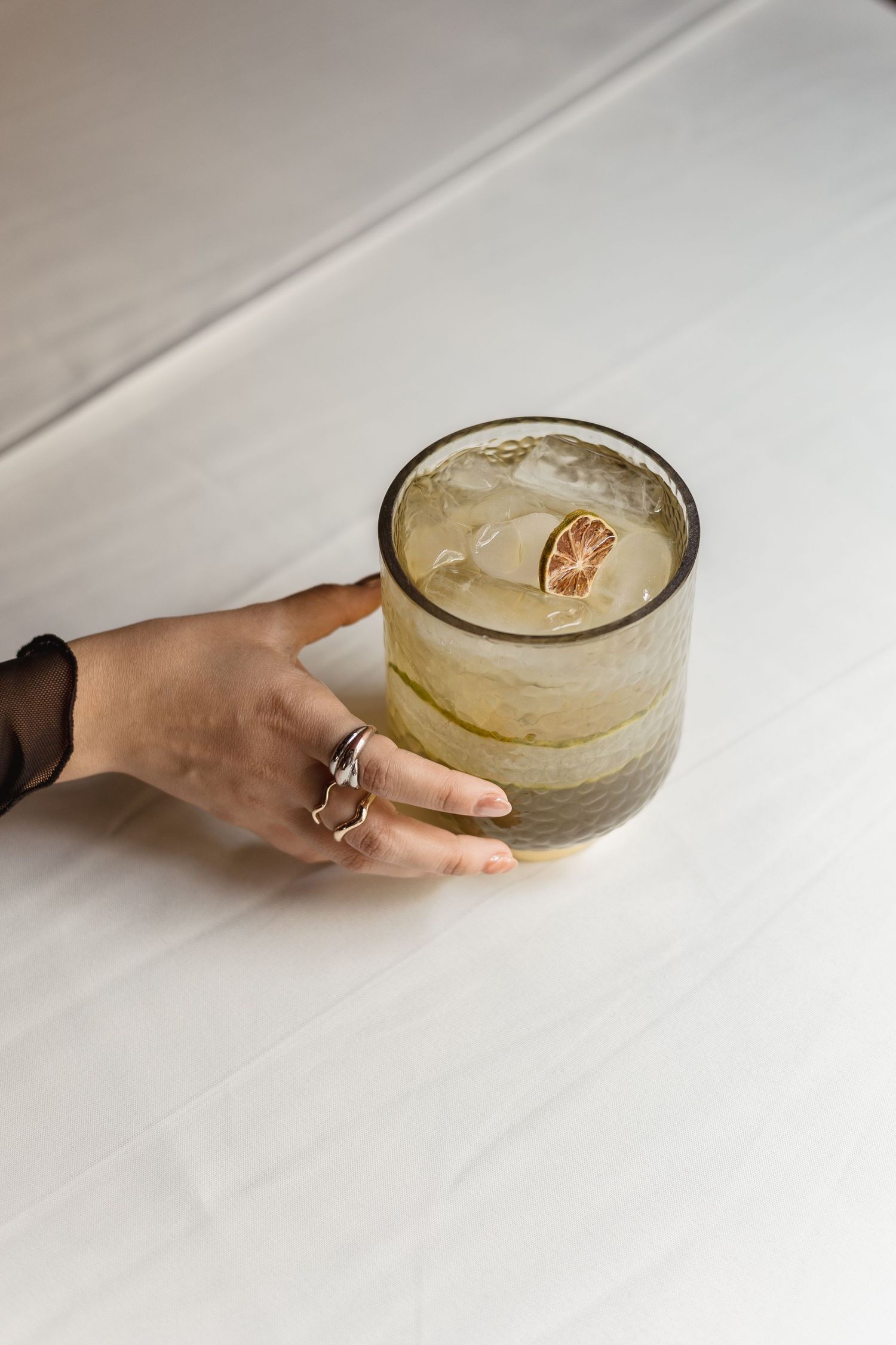 A hand reaches for a coupe glass filled with a creamy cocktail on a white surface.
