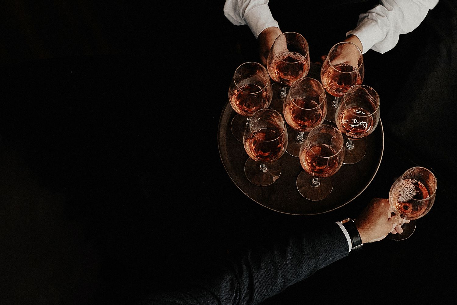 Multiple wine glasses being toasted in a dark setting with dramatic lighting and reflections.