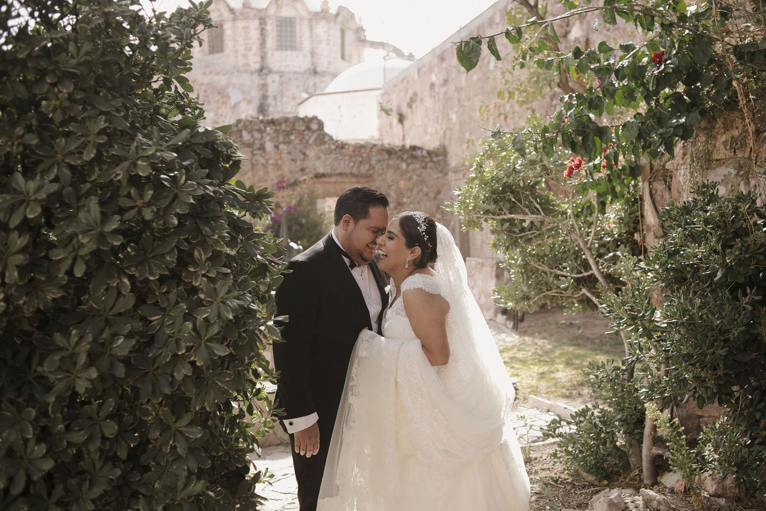 Newlyweds share an intimate moment in a garden path with historic architecture in the background.