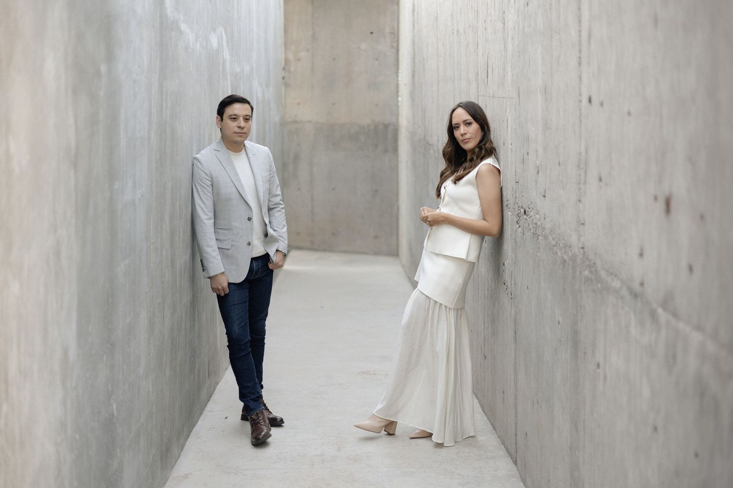 A couple poses for romantic wedding photos in a modern concrete hallway with dramatic lighting and shadows.