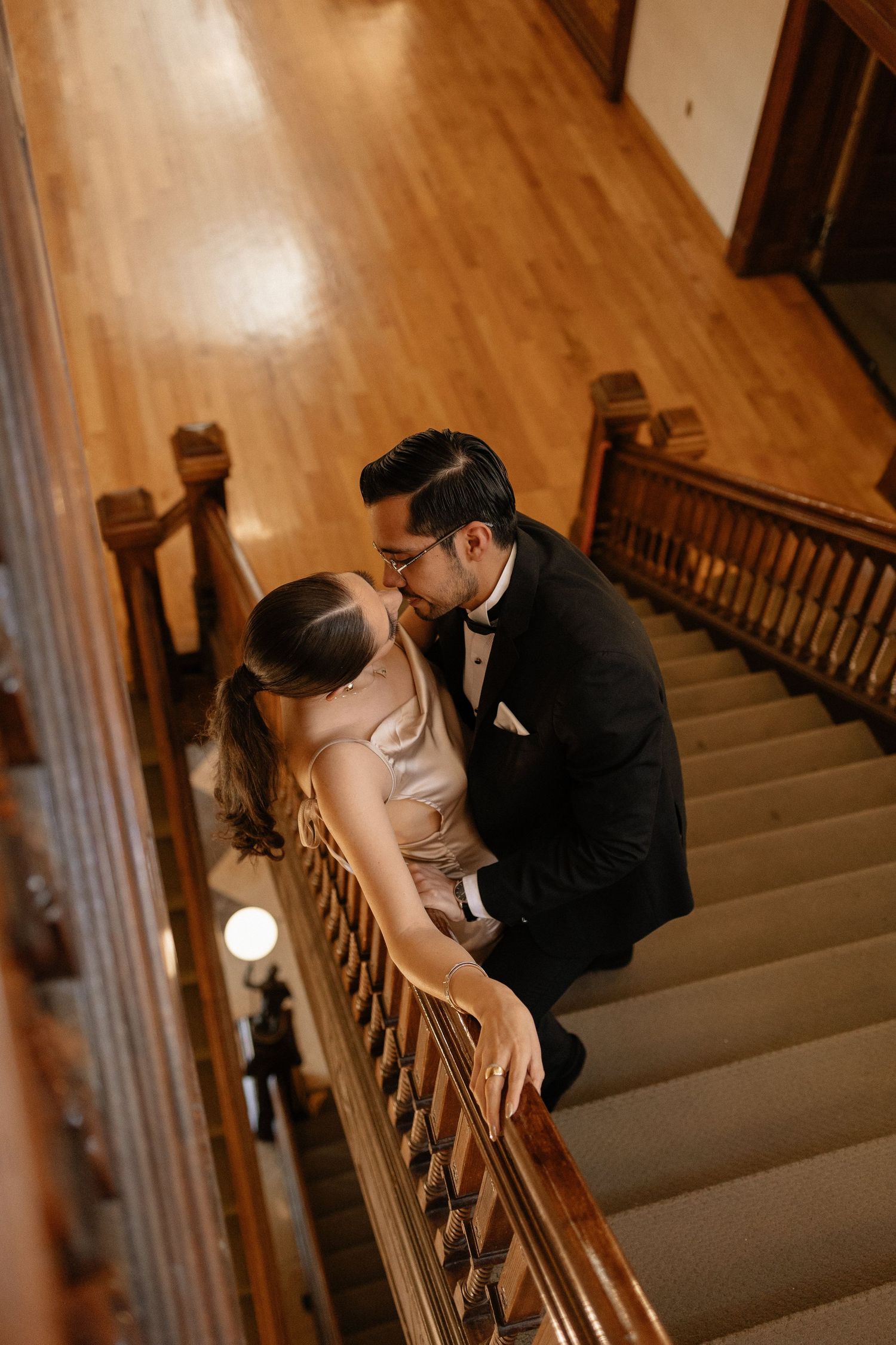 A romantic wedding couple shares an intimate moment on a wooden staircase in warm lighting.