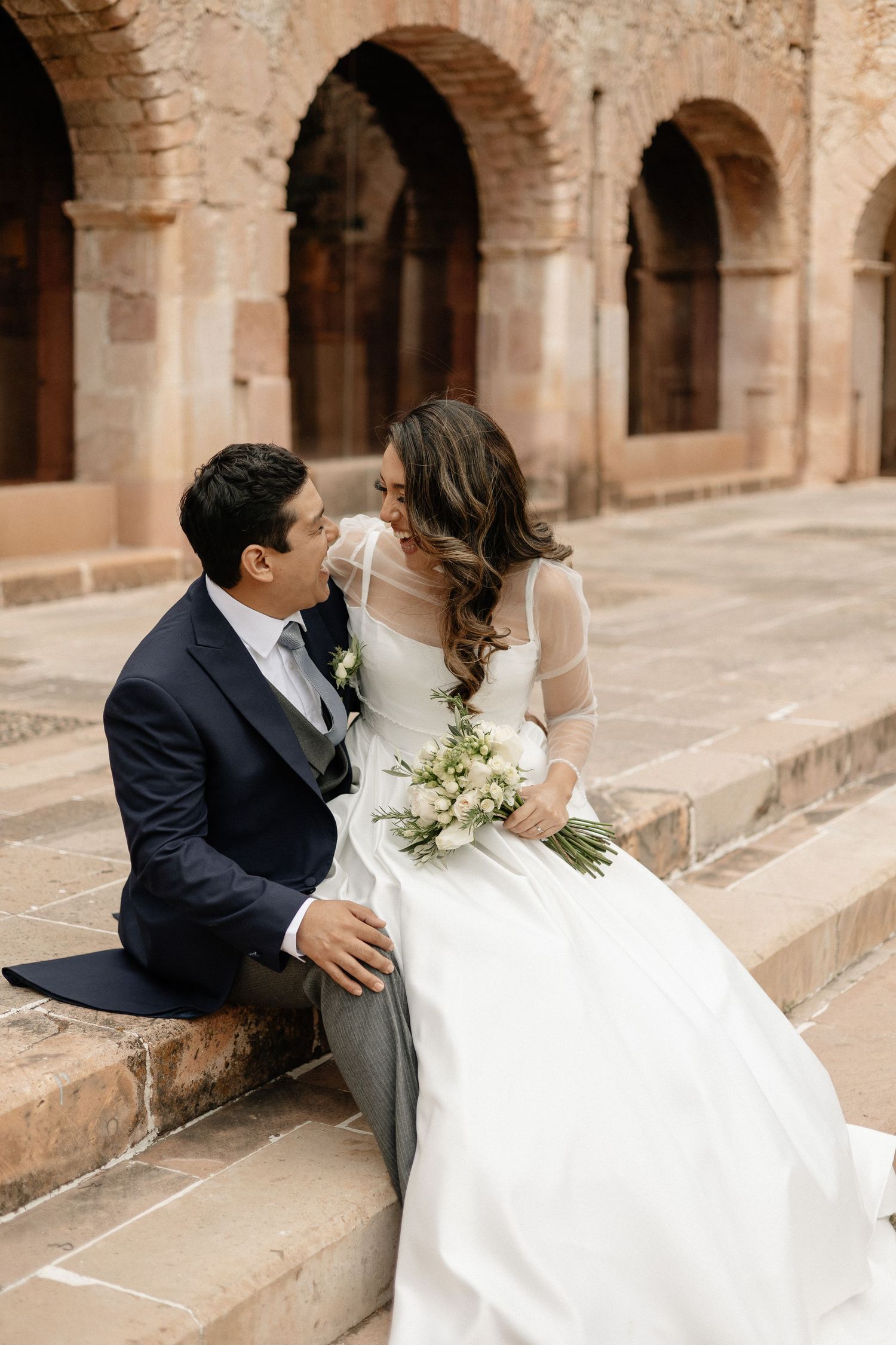 Romantic wedding couple shares intimate moments on stone steps of historic arched colonnade.
