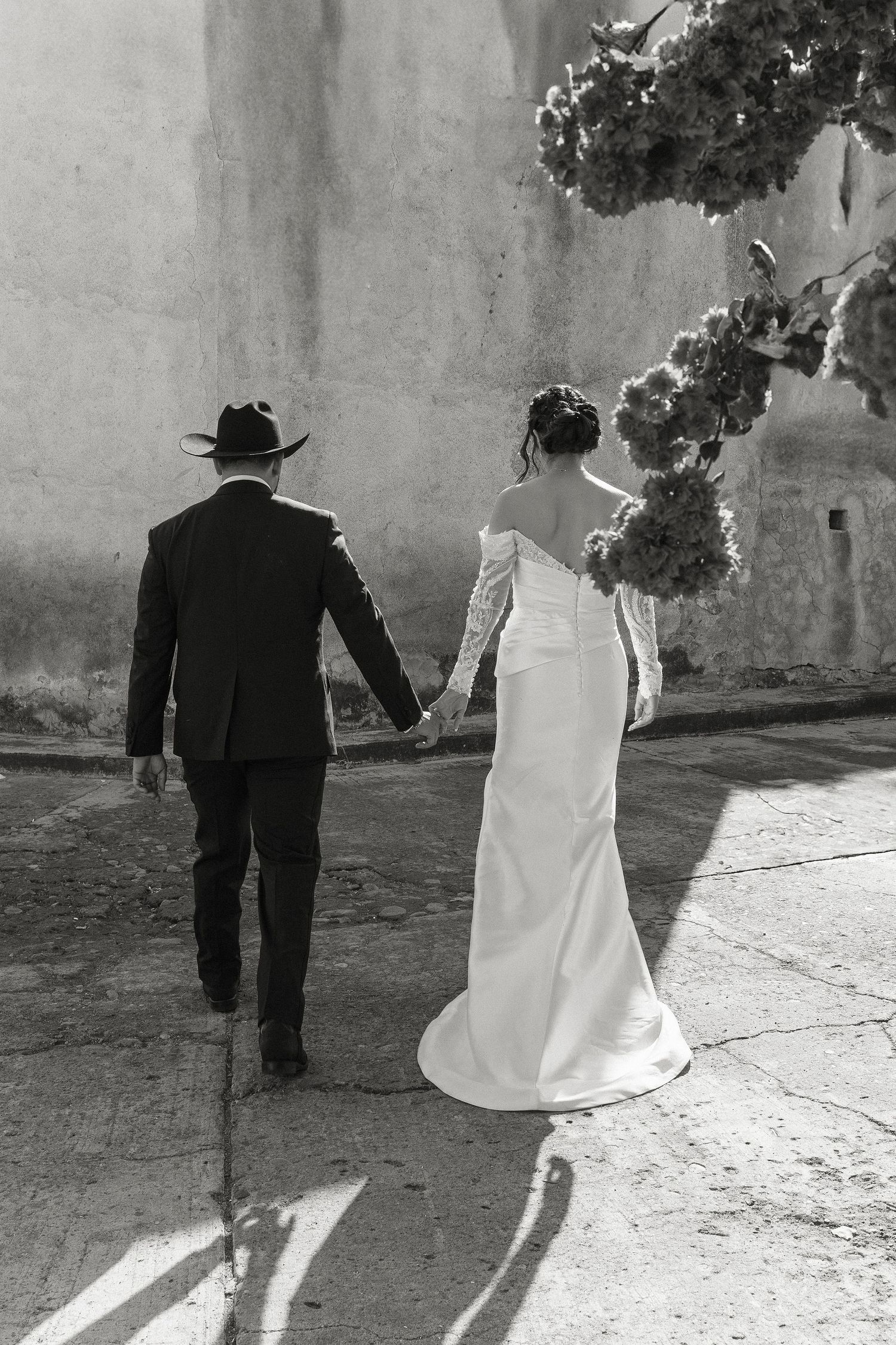 Black and white wedding photo series showing couple walking away together casting long shadows on stone pathway.