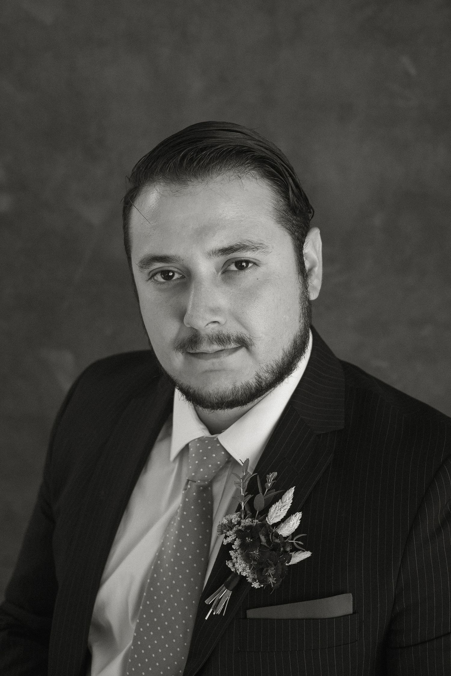 Black and white formal portrait of a person wearing a pinstriped suit with a polka dot tie and floral boutonniere.