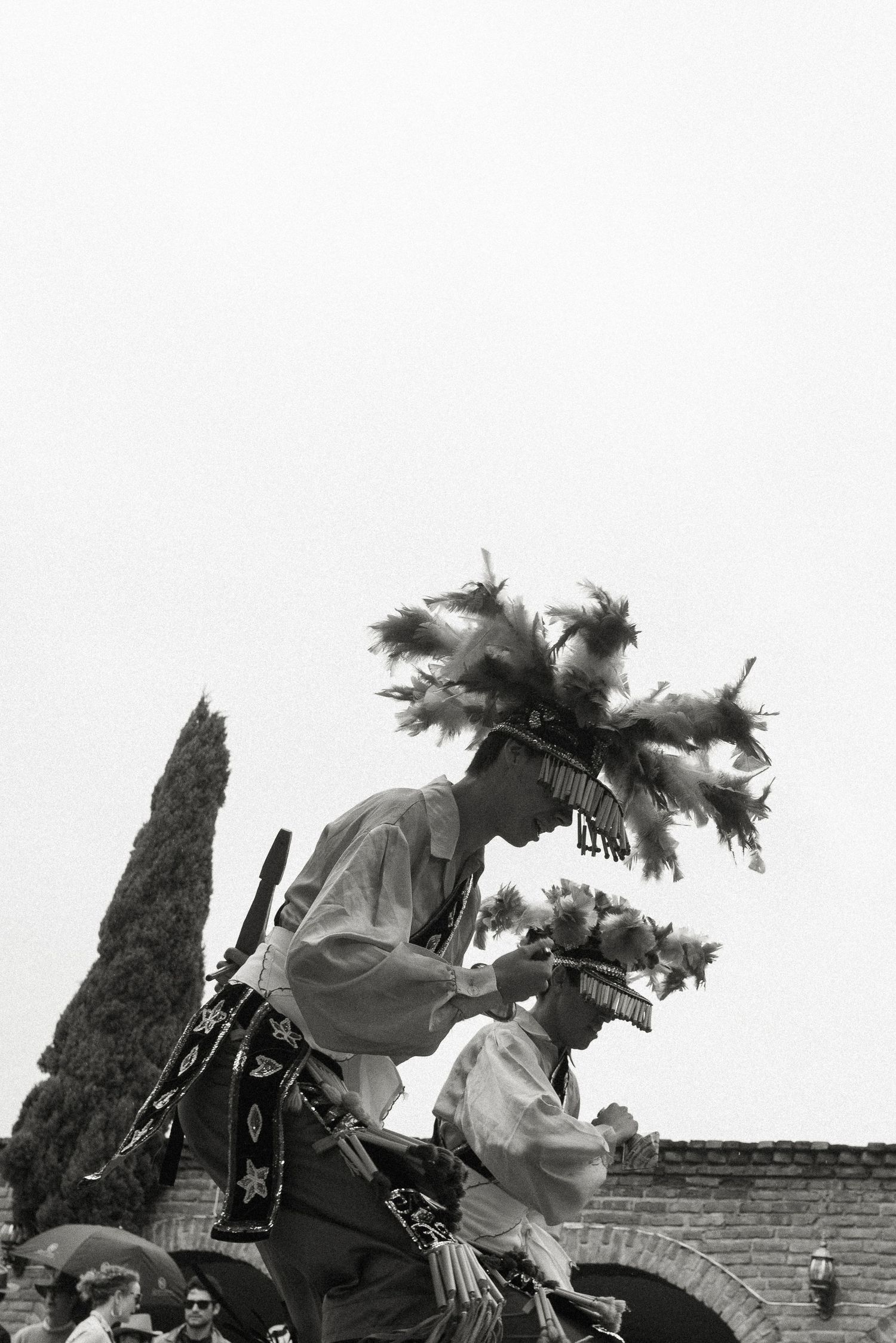 Black and white photo of dancers wearing traditional Native American regalia performing at an outdoor ceremony.