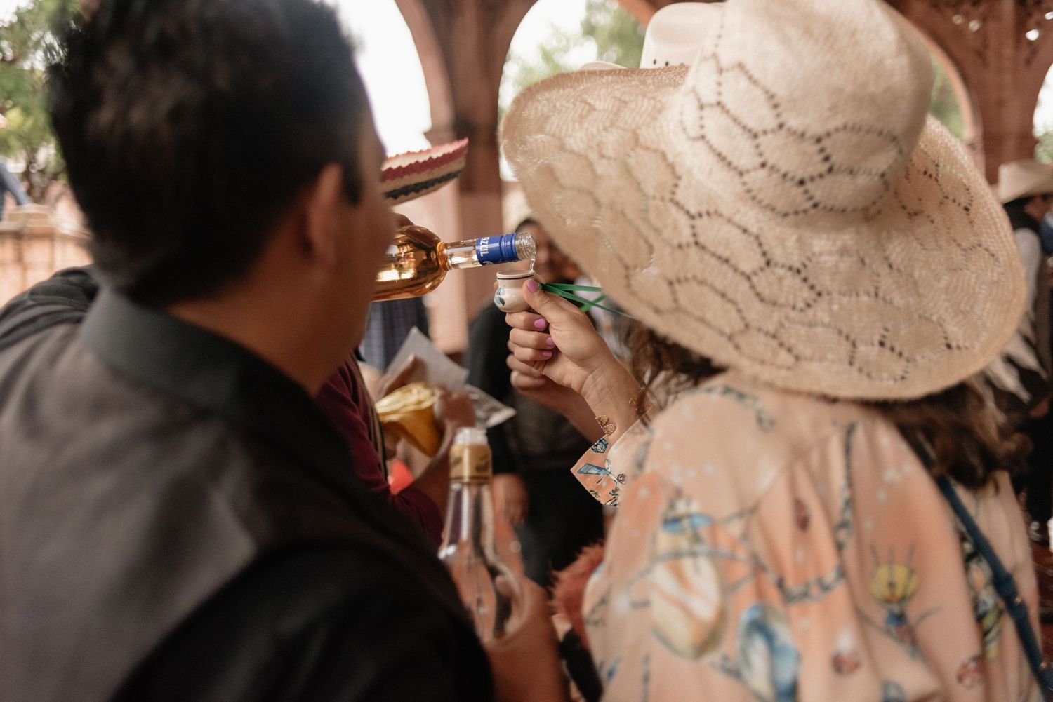 Two people sharing a refreshing drink from a bottle at an outdoor gathering.
