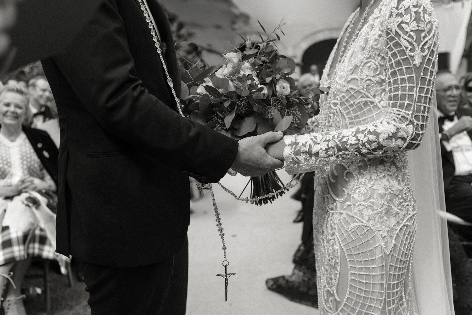 A black and white wedding photograph showing the exchange of bouquet between two people wearing formal attire.