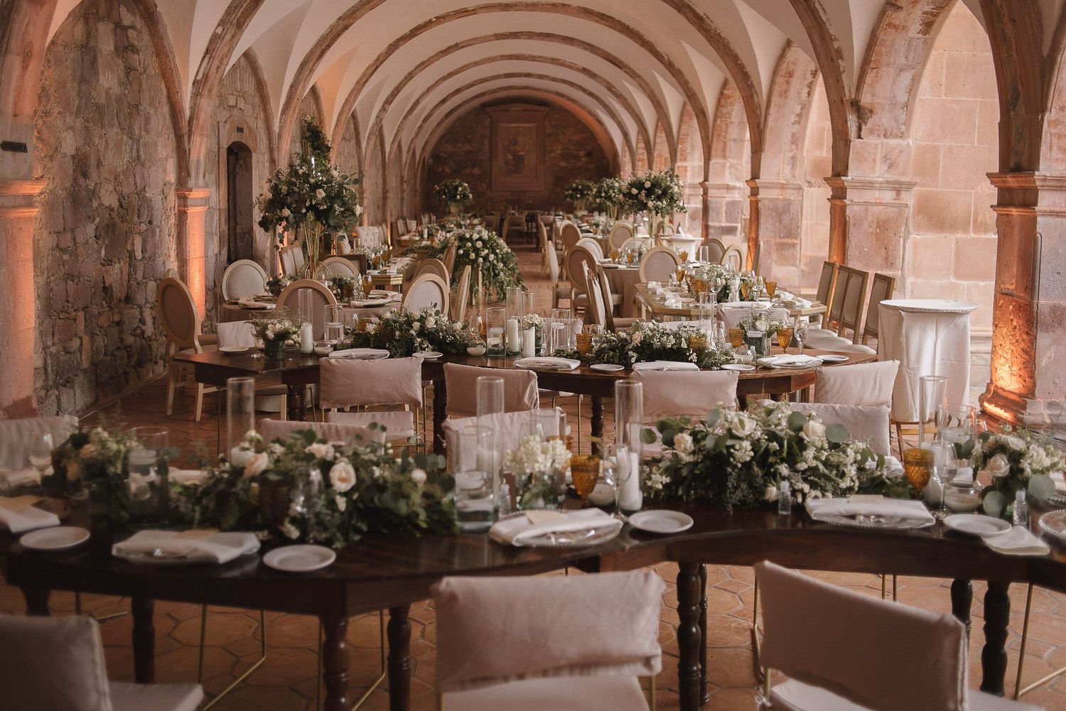 Elegant wedding reception table setup in a vaulted stone room with floral arrangements and candles.