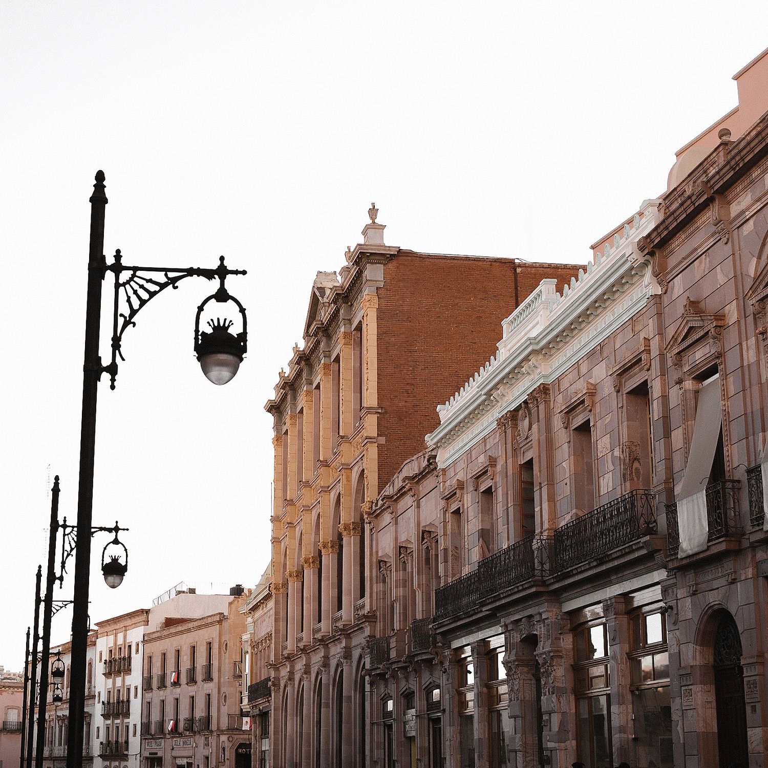 Historic colonial architecture lines a street with ornate lamp posts in Zacatecas, Mexico, featuring orange and white buildings.