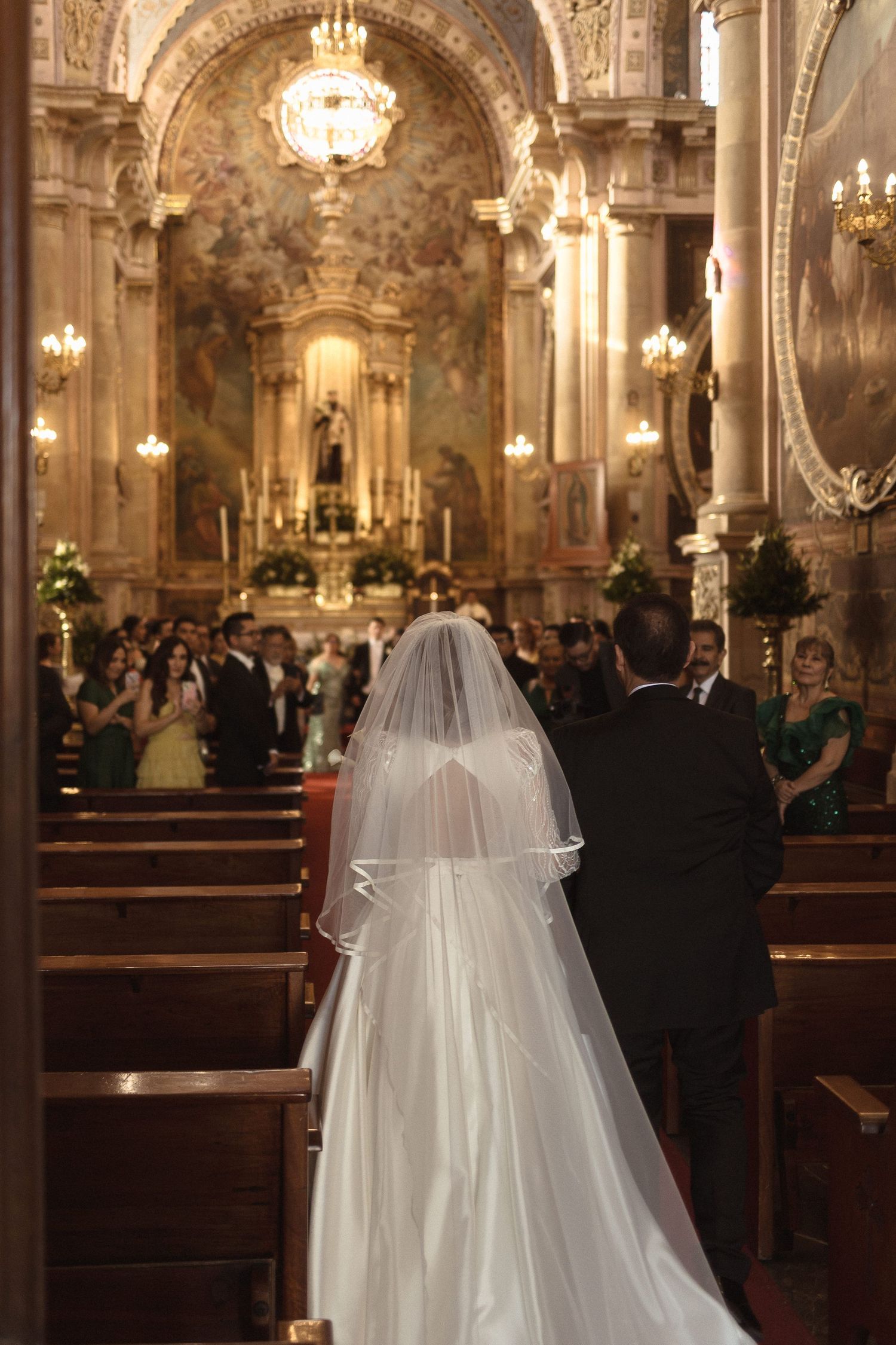 A wedding ceremony in a grand ornate cathedral with crystal chandeliers and guests seated in wooden pews.