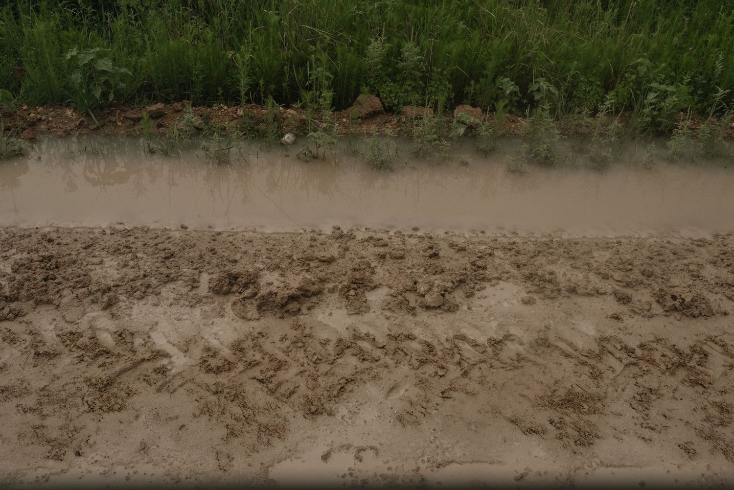 Muddy brown water churns and creates turbulent patterns along a dirt riverbank on a cloudy day.