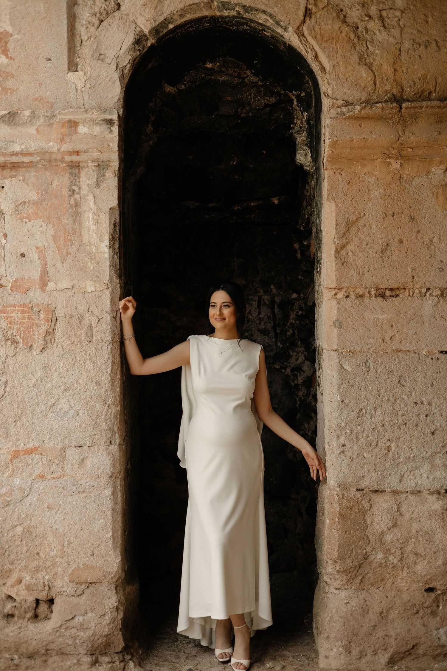 A series of four artistic photos showing a white dress against stone archways and textured walls.
