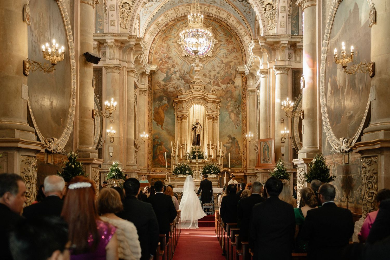 Elegant baroque palace interior with ornate chandeliers and gilded details during a formal gathering.