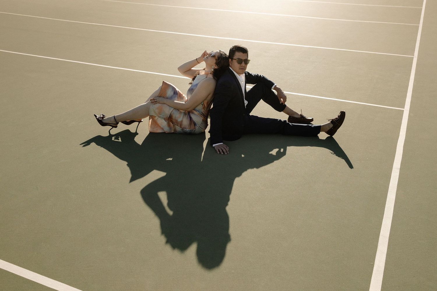 Two dancers perform a synchronized pose on the floor casting dramatic shadows in a studio setting.