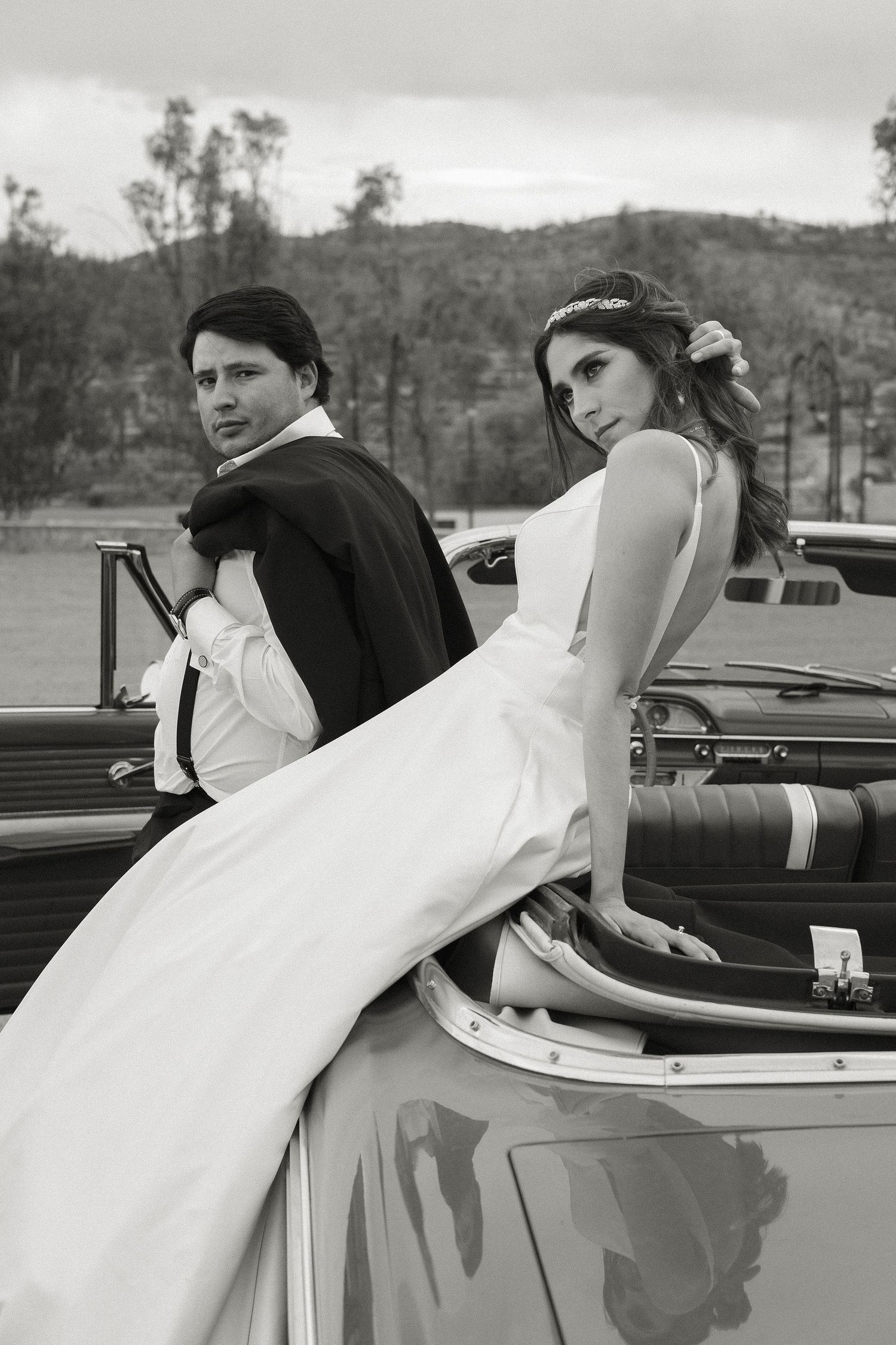 Classic white wedding dress flowing over the side of a vintage convertible car.