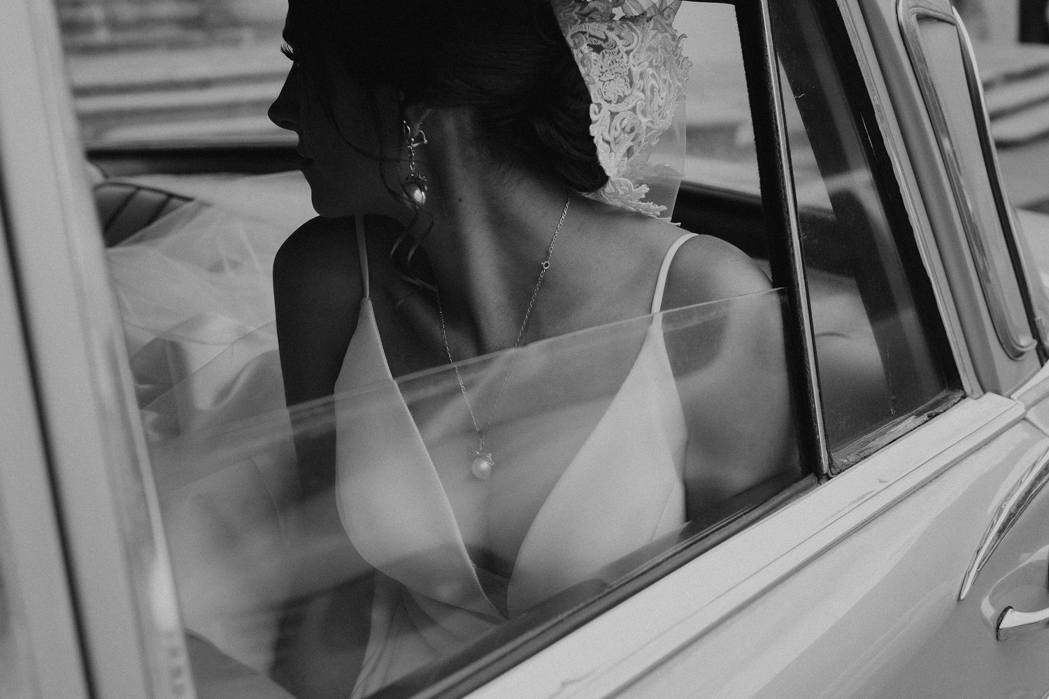 Vintage black and white photograph of a passenger looking out of a car window on a city street.