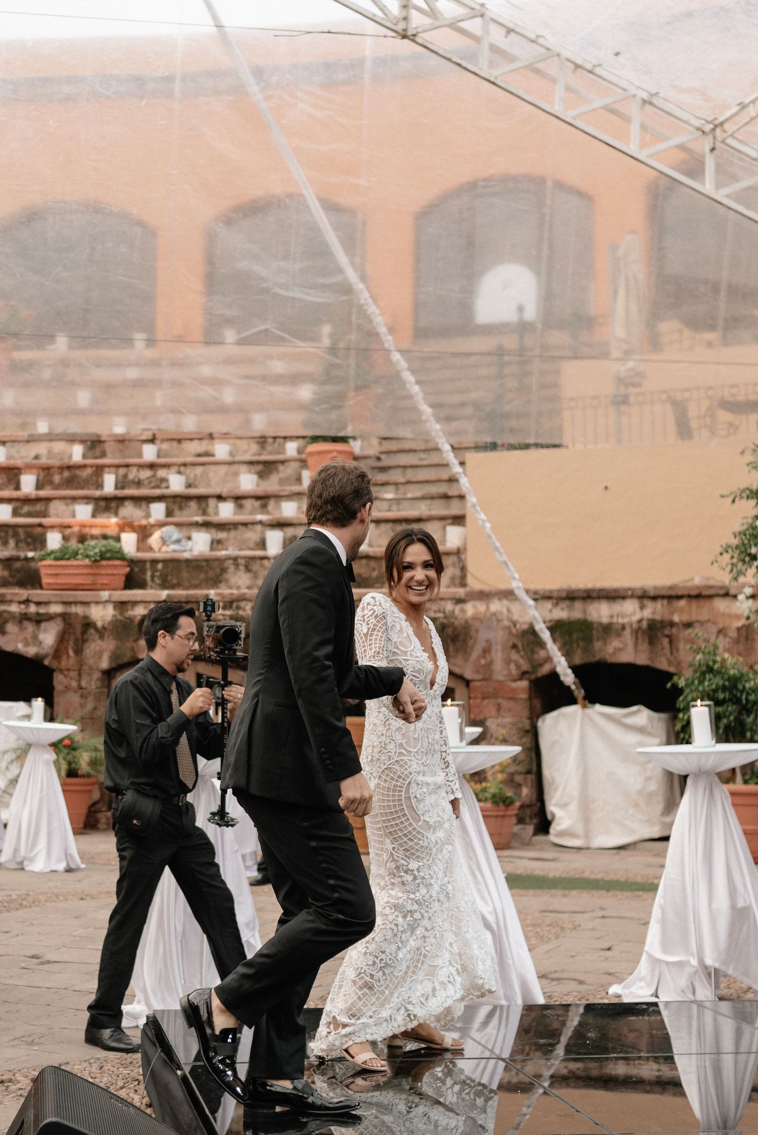 People dancing at an elegant outdoor wedding celebration with stone architecture and white fabric decorations in background.
