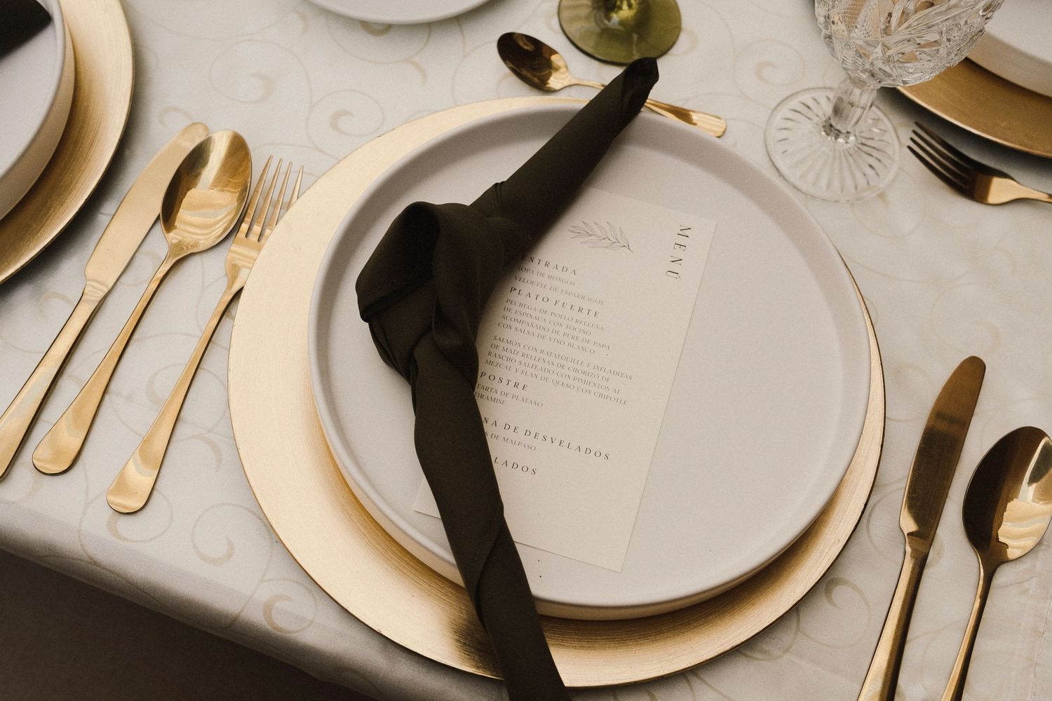 Elegant place setting with gold cutlery, white plates and black napkin on marble table.
