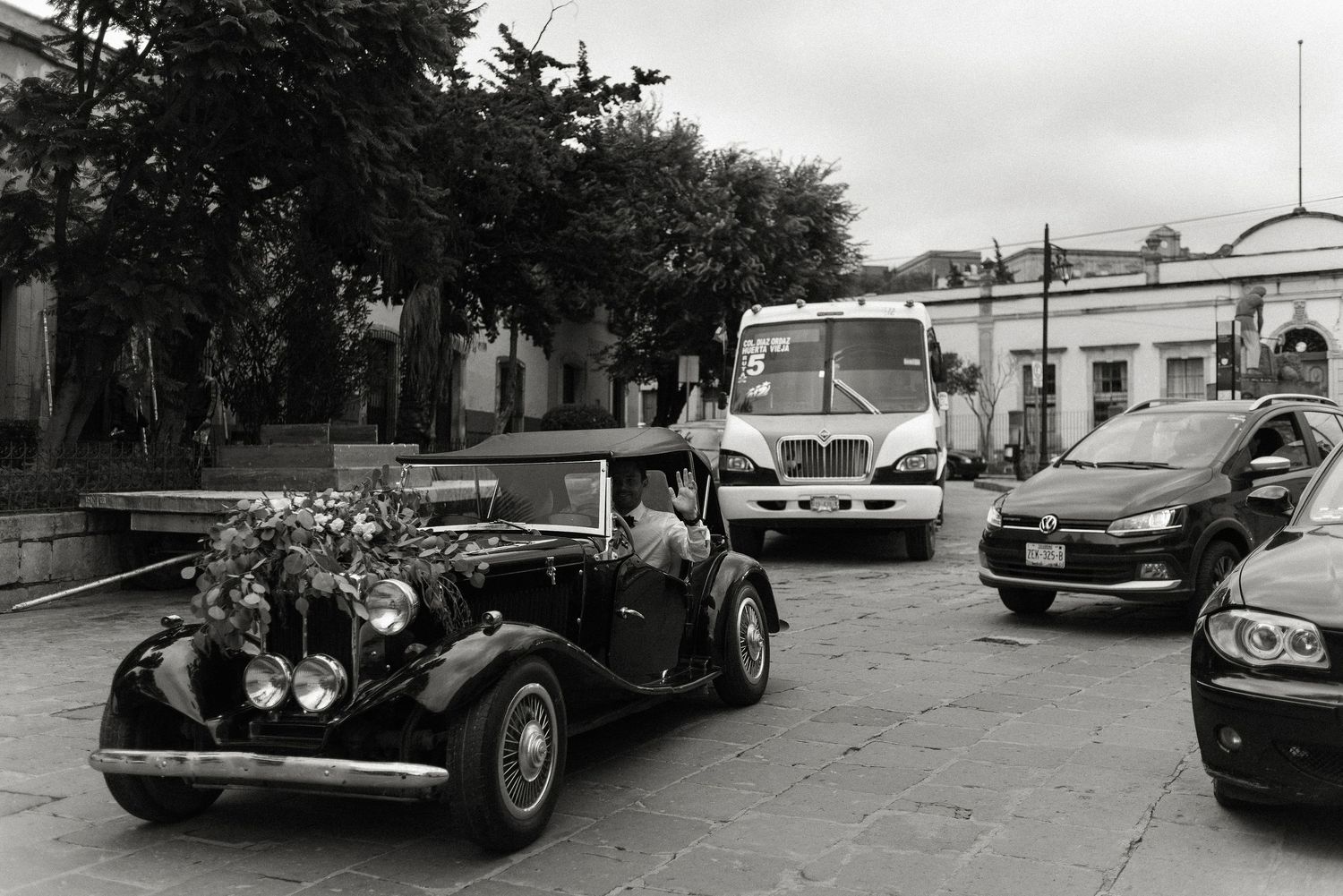 A vintage classic car parked on a street alongside modern vehicles in black and white photography.