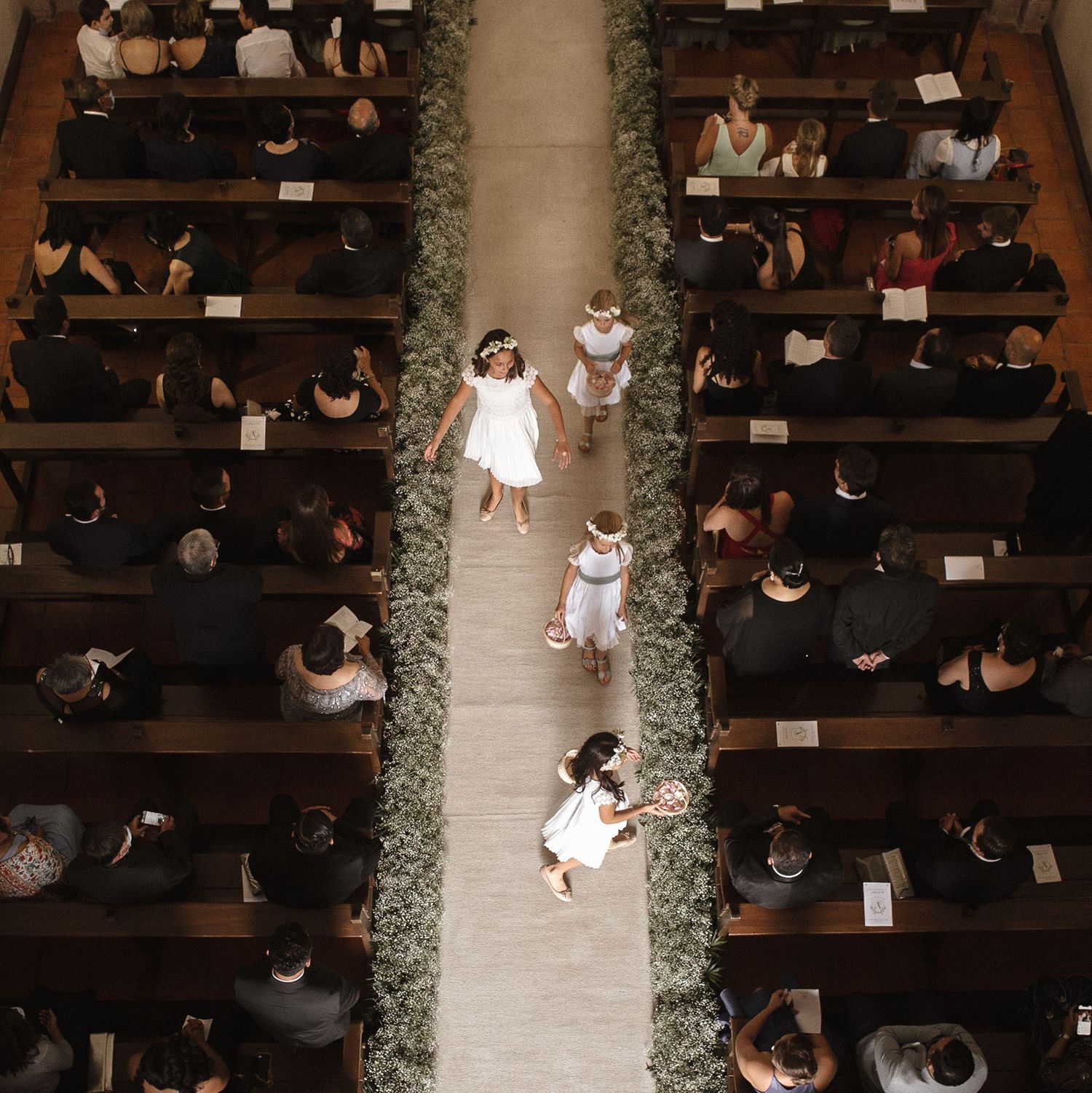 Overhead view of wedding guests seated in wooden church pews during a ceremony.