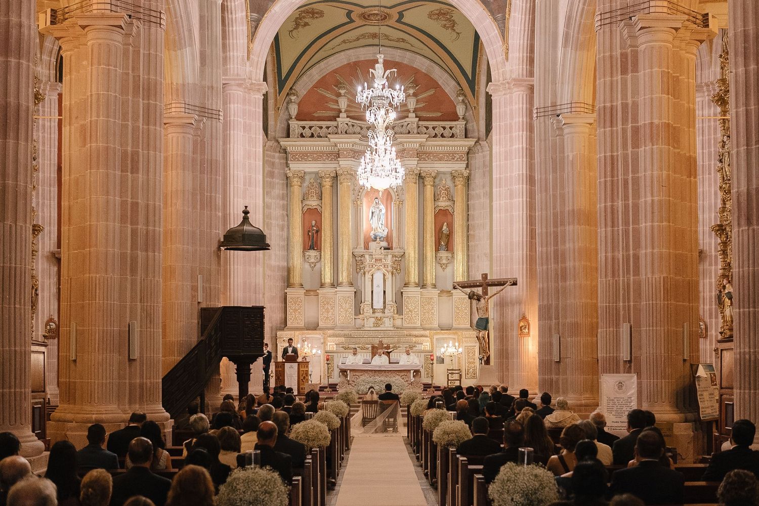 Grand cathedral interior with ornate columns and chandeliers during wedding ceremony.