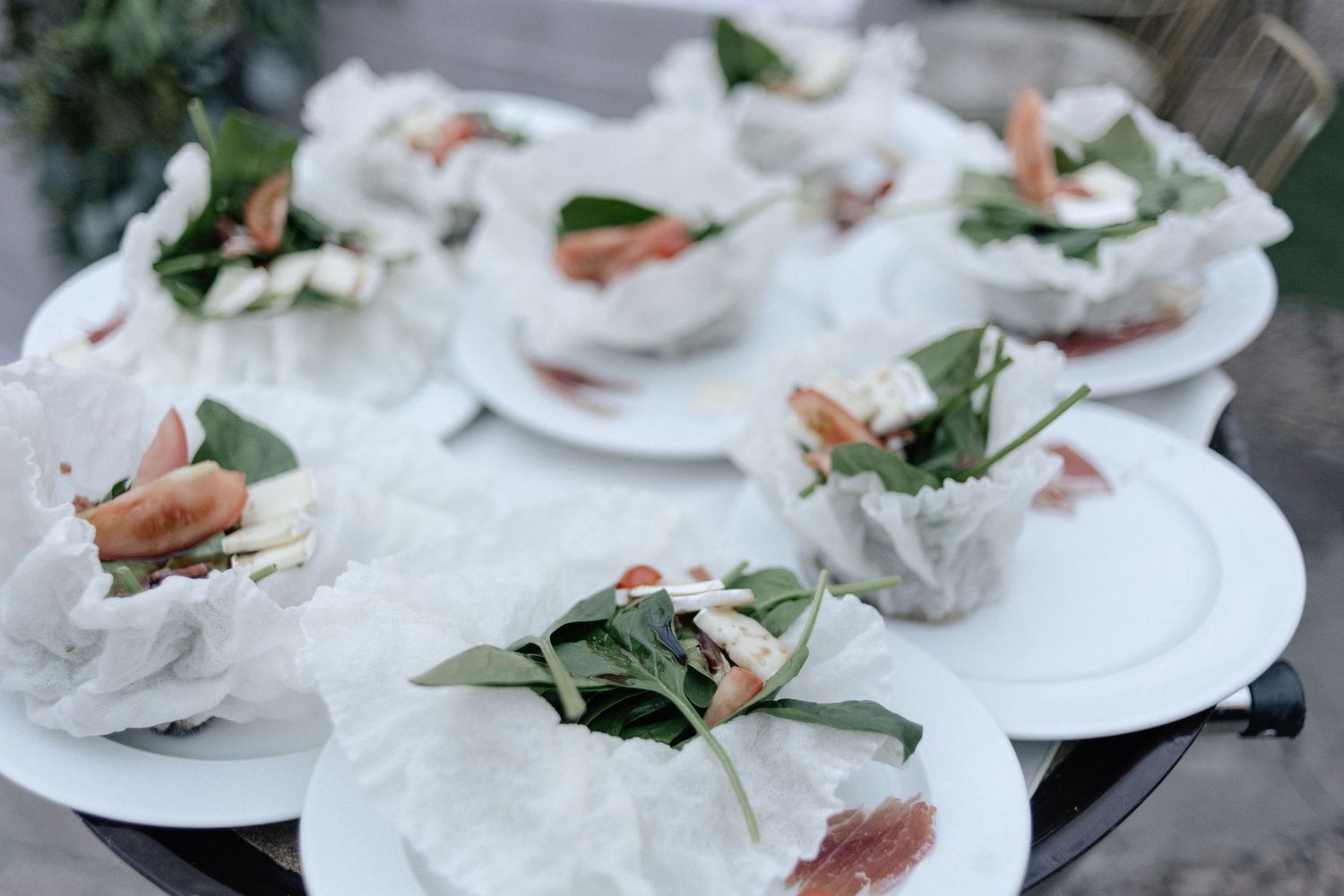 Individual place settings with fresh greens and delicate ingredients arranged on white plates with translucent wrappings.