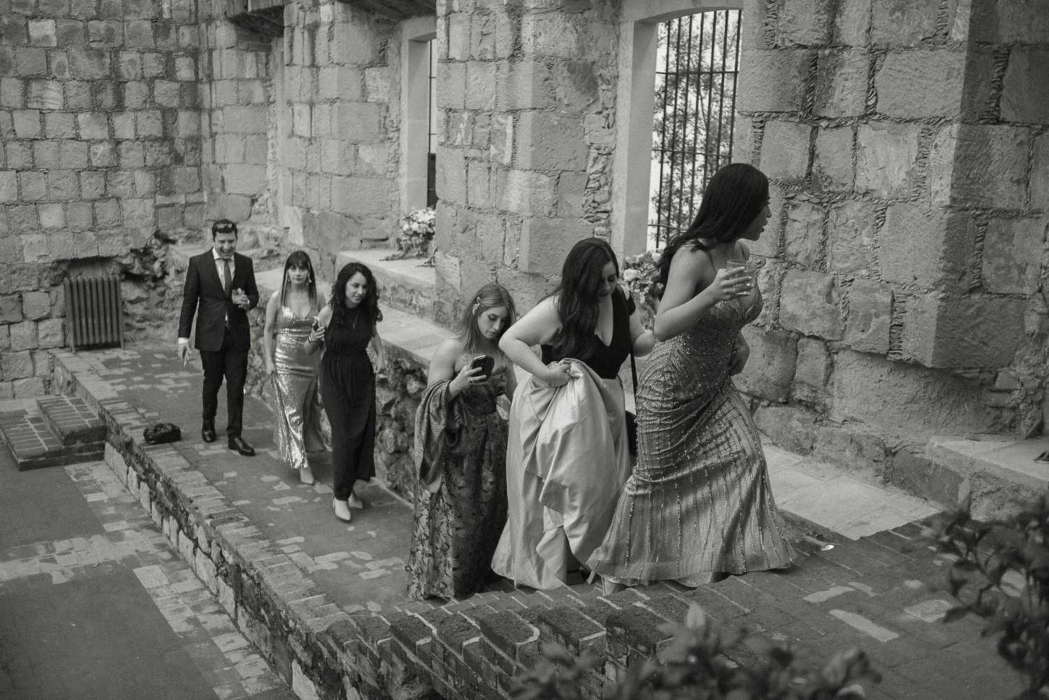 Wedding party walking along stone walls in formal attire.