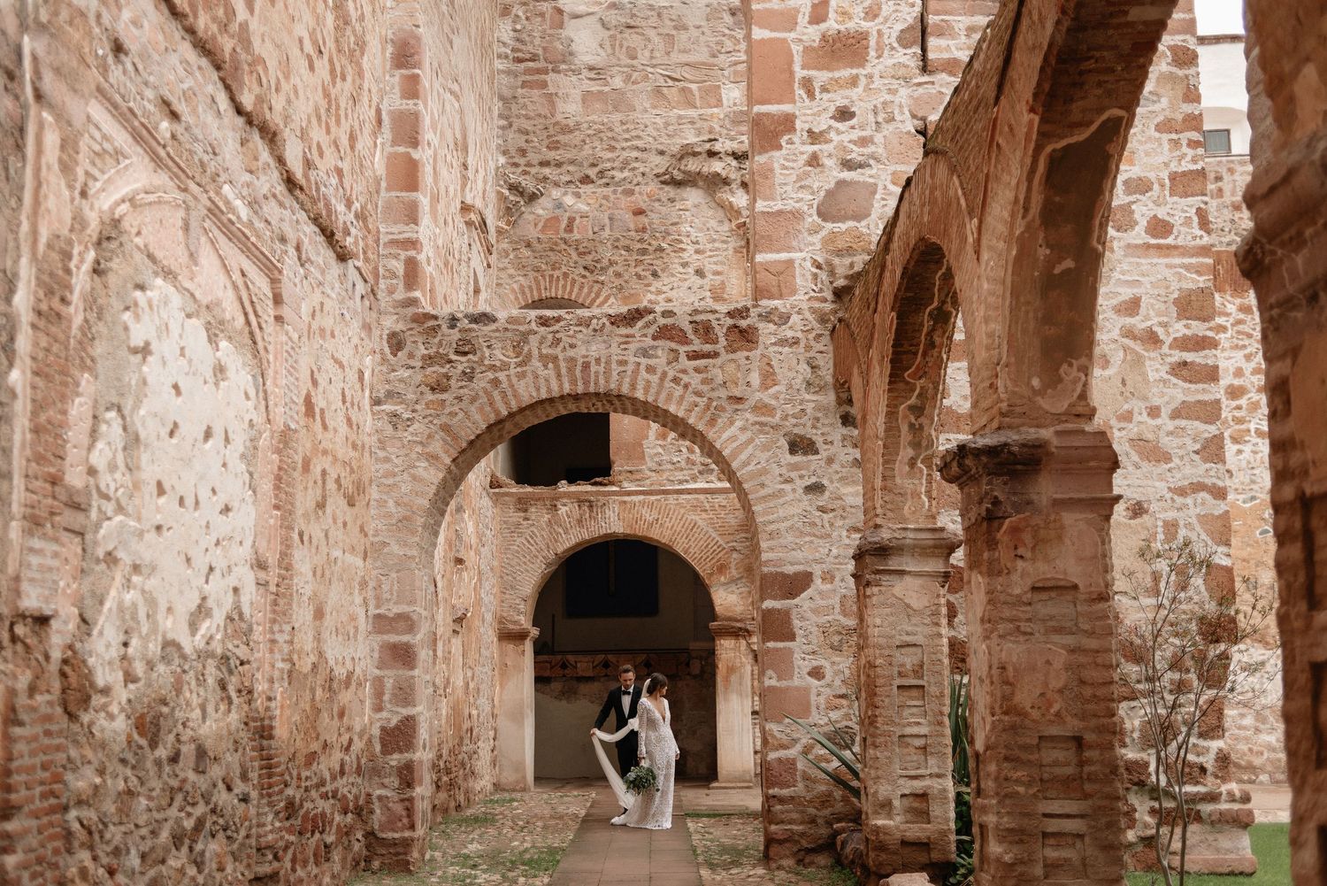 Couple stands in archway of ancient stone ruins with exposed brick walls and multiple arched passageways.