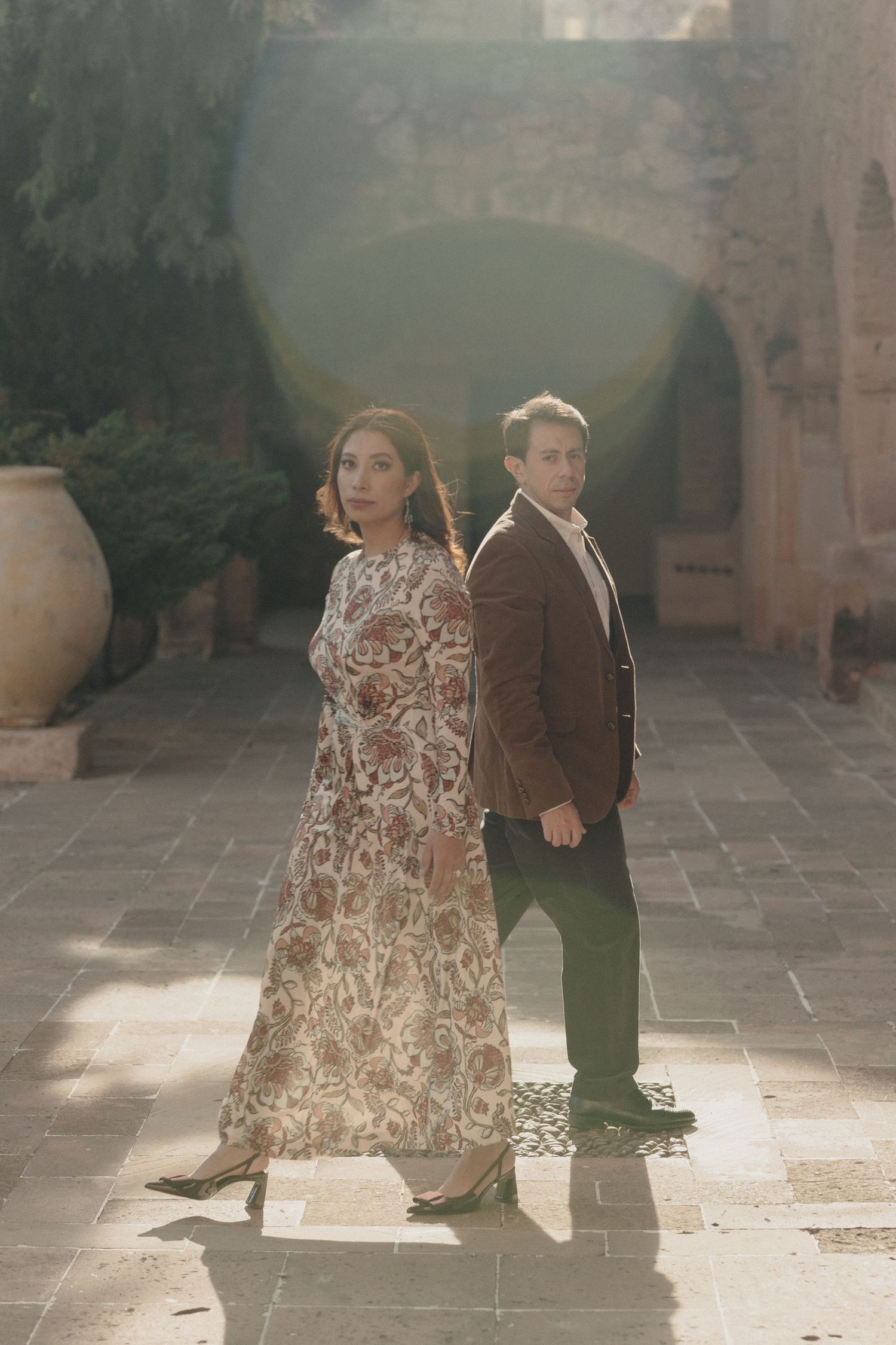 A couple in formal attire dances gracefully in a sunlit courtyard with stone architecture.