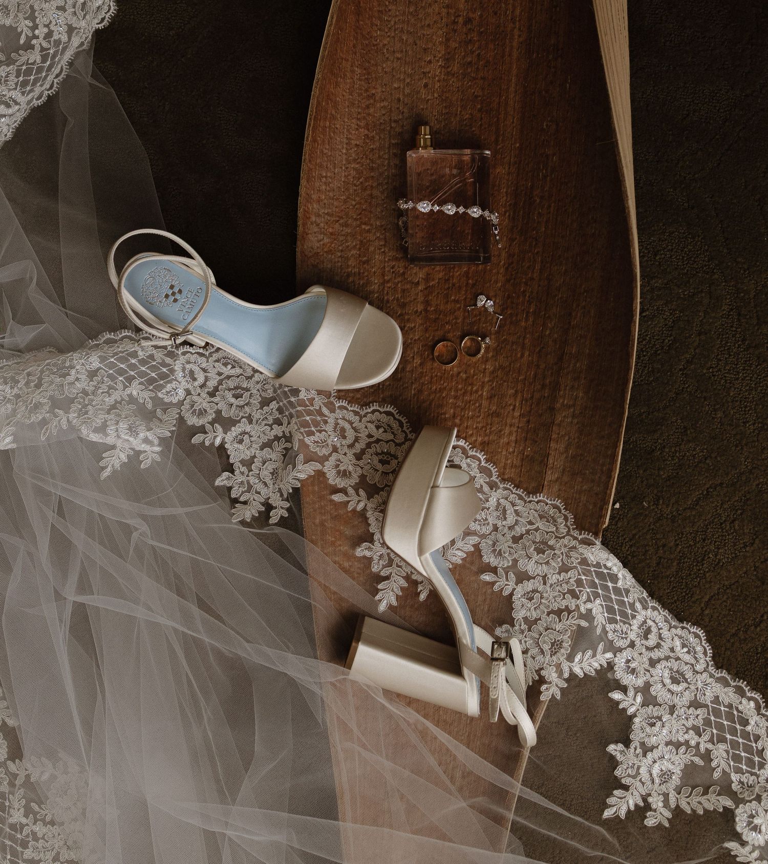 White lace wedding dress with delicate veil details draped over wooden furniture in soft lighting.