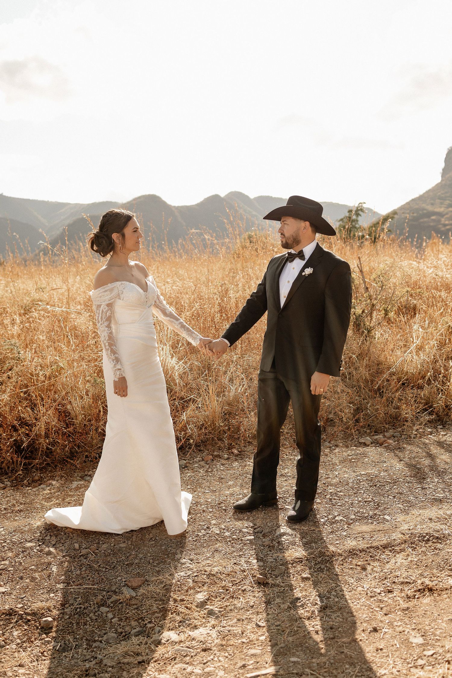 Bride and groom dance playfully in a golden field at sunset with mountains in the background.
