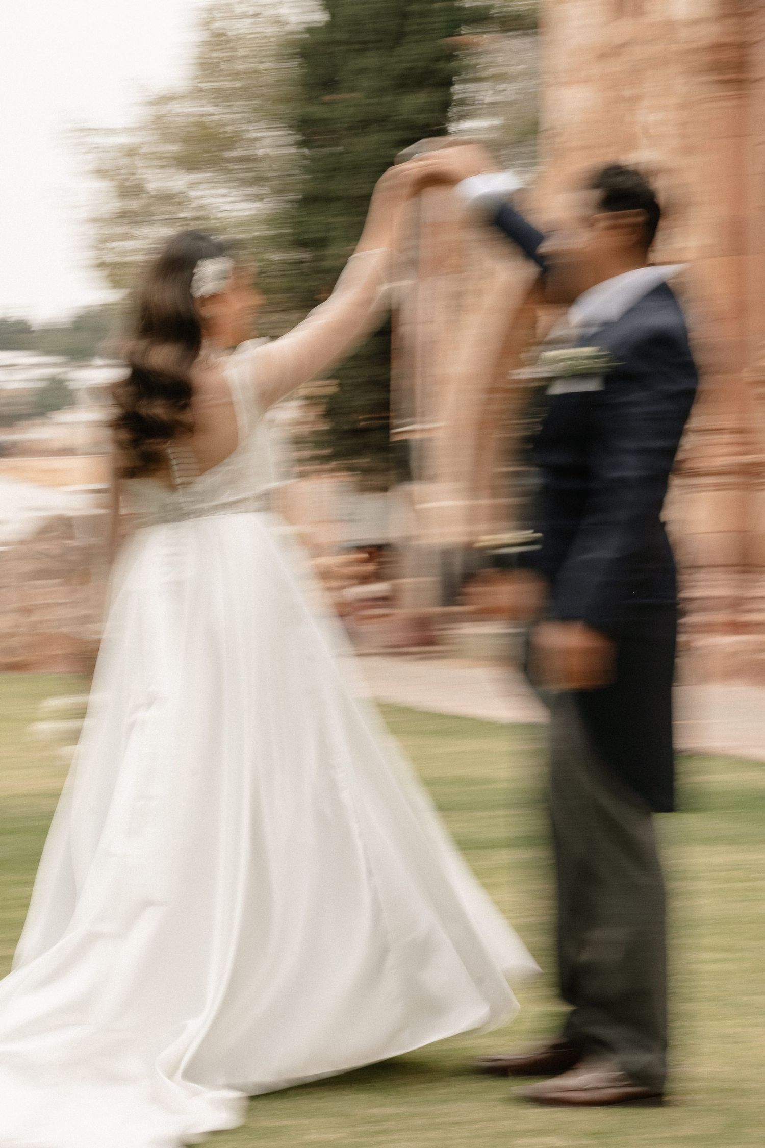 Motion-blurred sequence of a couple dancing at an outdoor wedding, showing flowing white dress and dark suit.