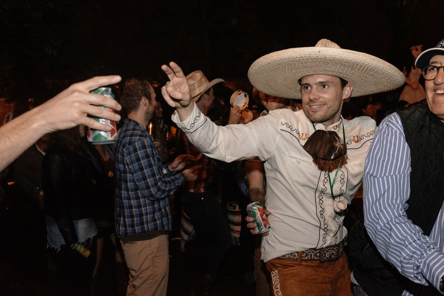 Someone in a sombrero and traditional Mexican attire dances at what appears to be a festive nighttime gathering.