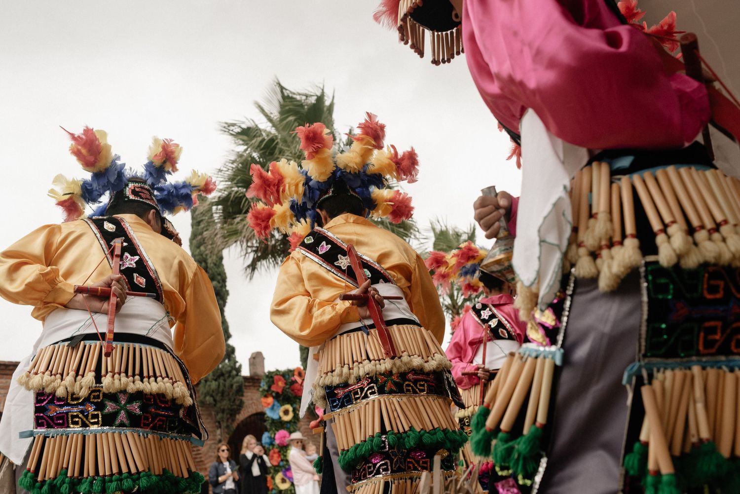 Traditional indigenous dancers wearing straw costumes adorned with colorful feathers perform at a cultural celebration.